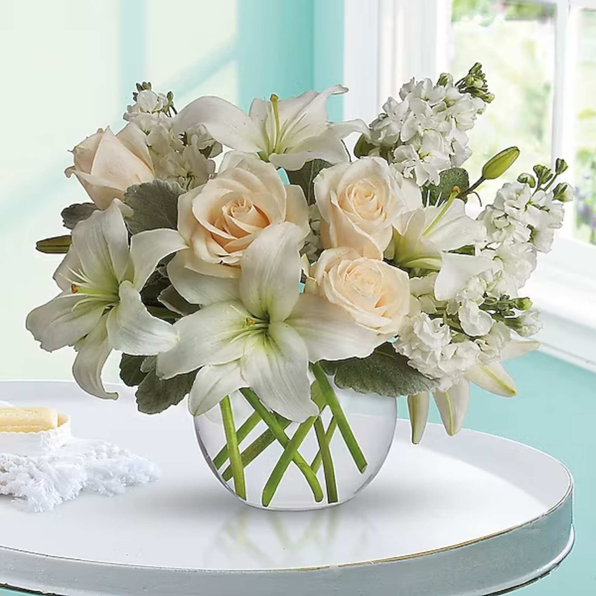 Cream roses and white lilies arranged in a clear glass vase