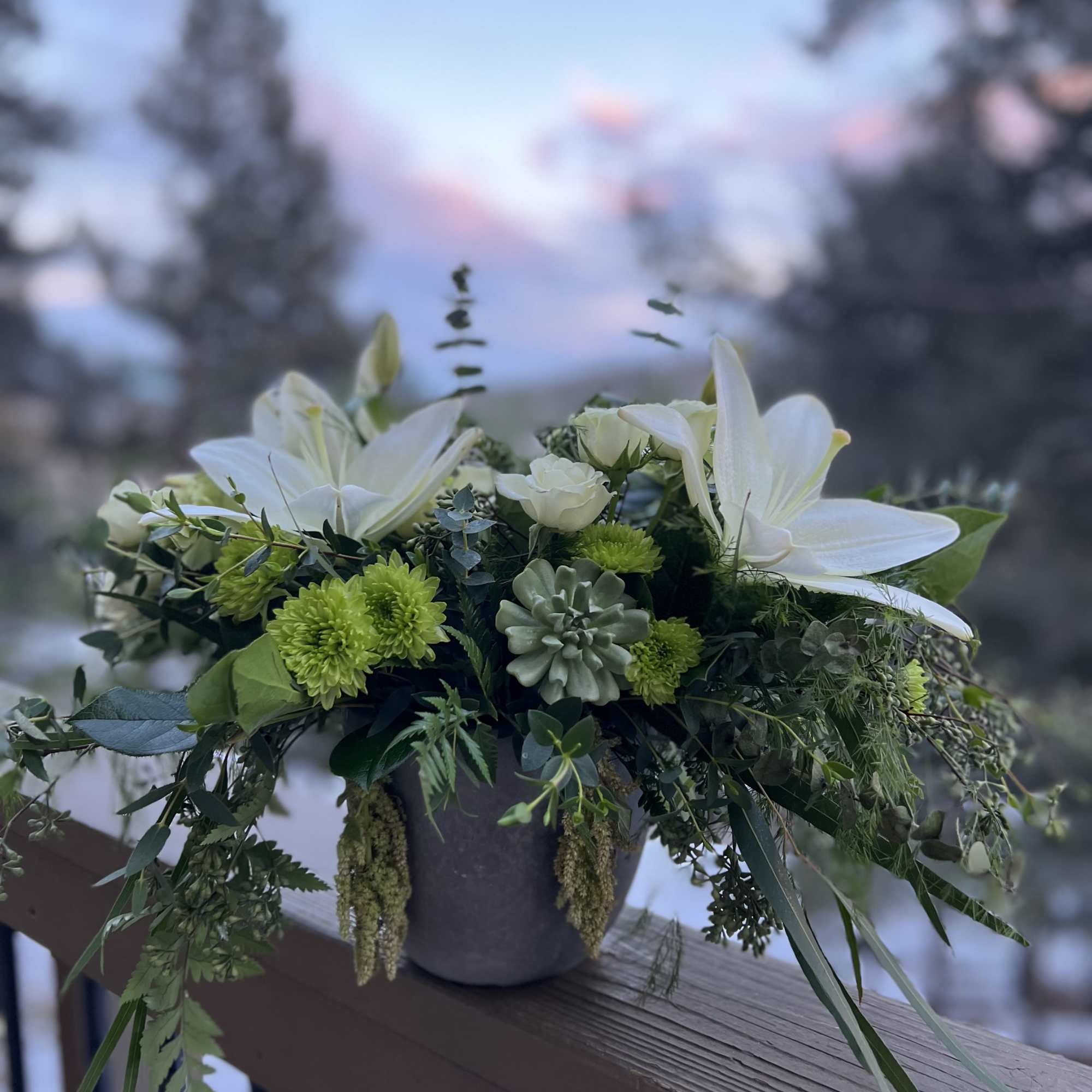 White lilies and green chrysanthemums in a gray vase with trailing greenery