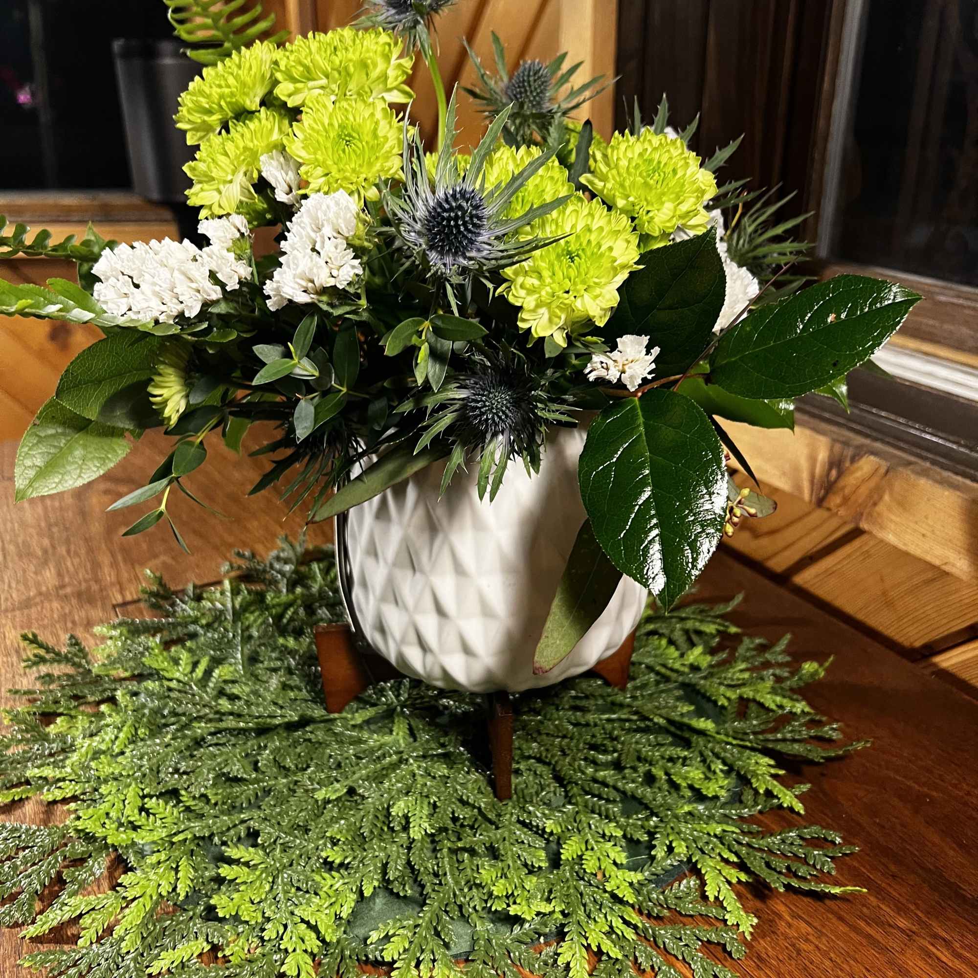 White and lime-green flowers in a white vase with spiky blue thistles