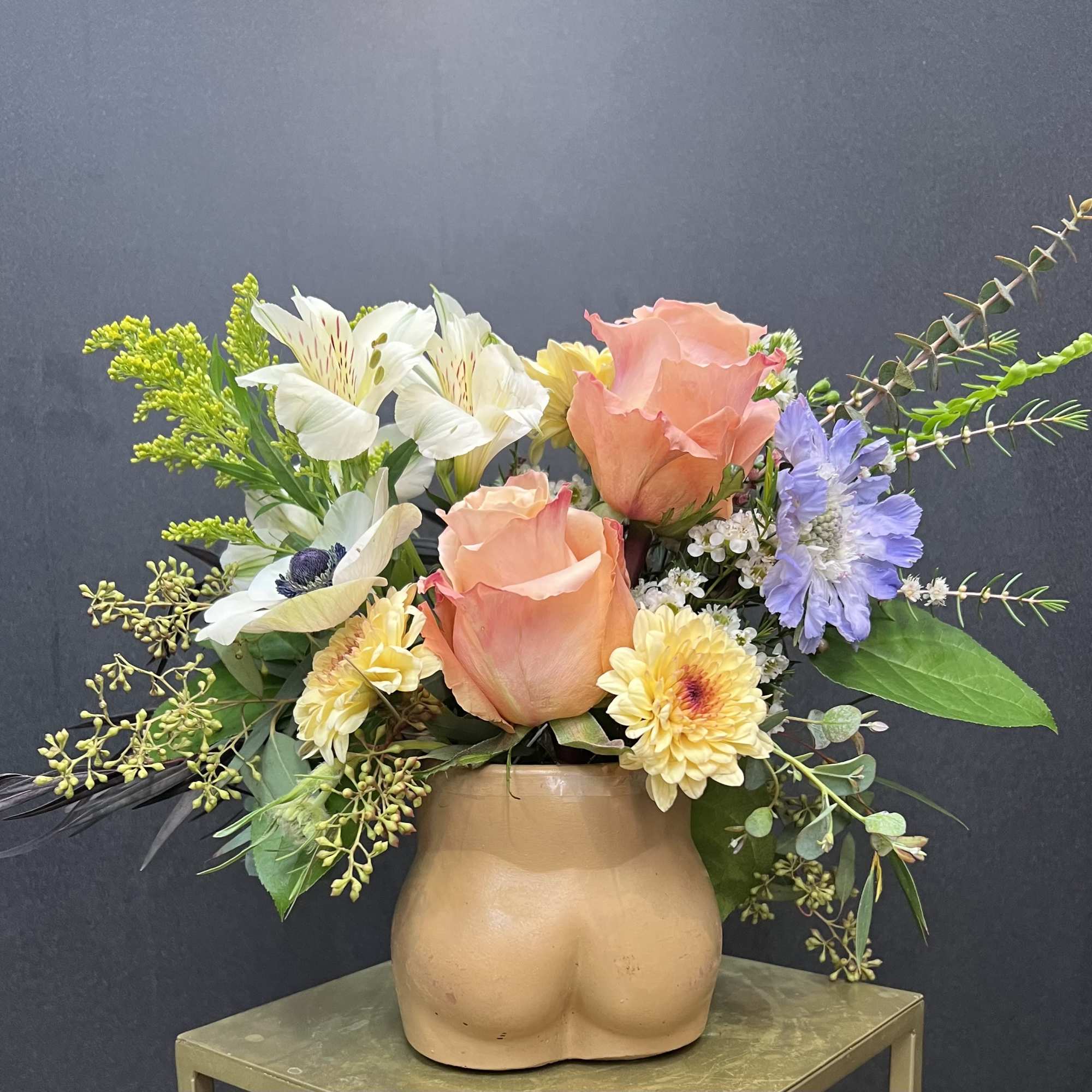 Peach roses and mixed flowers in a tan ceramic vase shaped like a torso