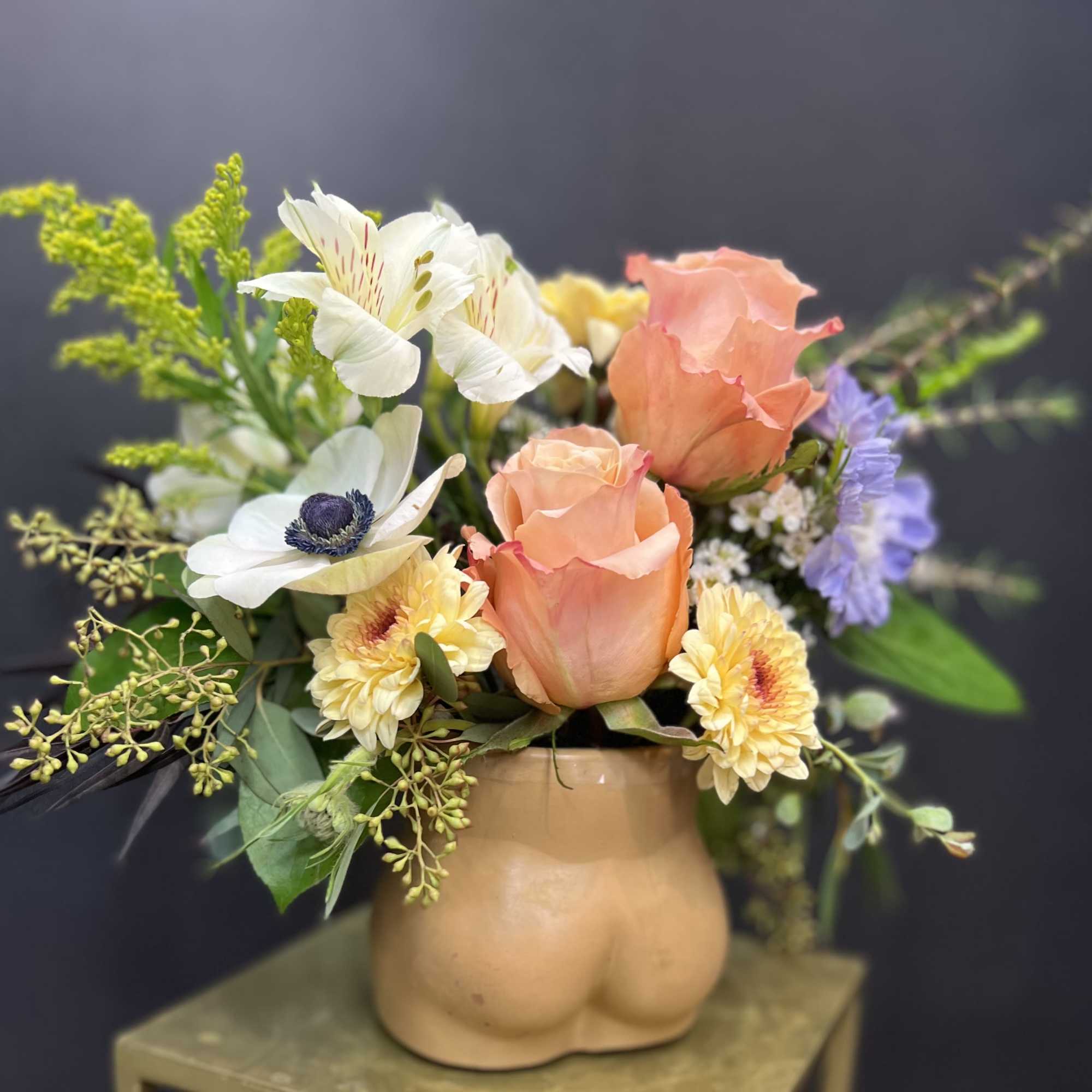 Peach roses and white flowers arranged in a tan ceramic vase