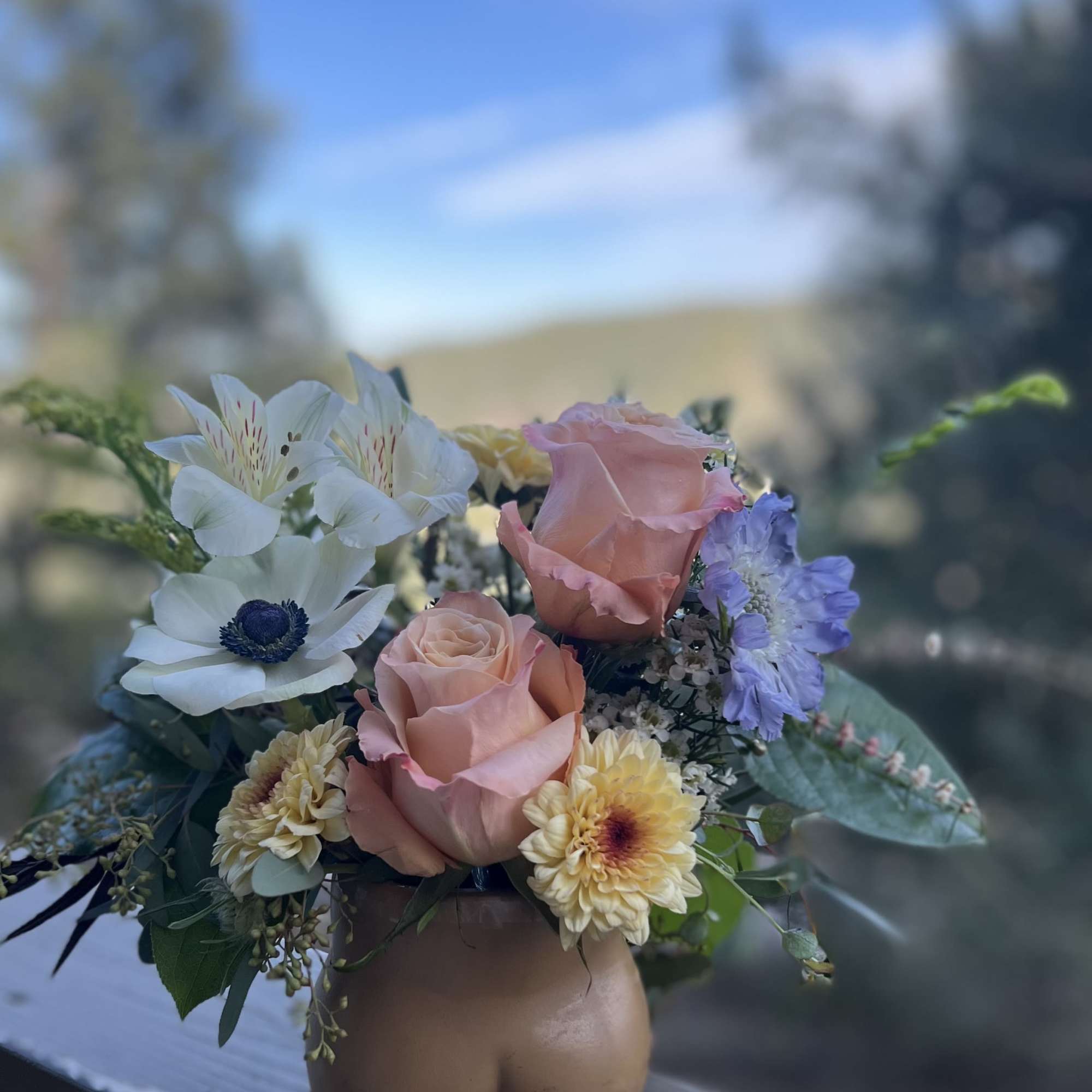Bouquet of pink roses, white anemones, and purple flowers in a vase
