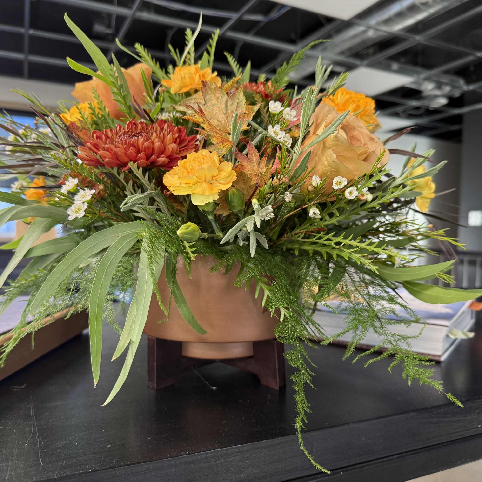 Autumn floral arrangement in a low round container with orange and red blooms