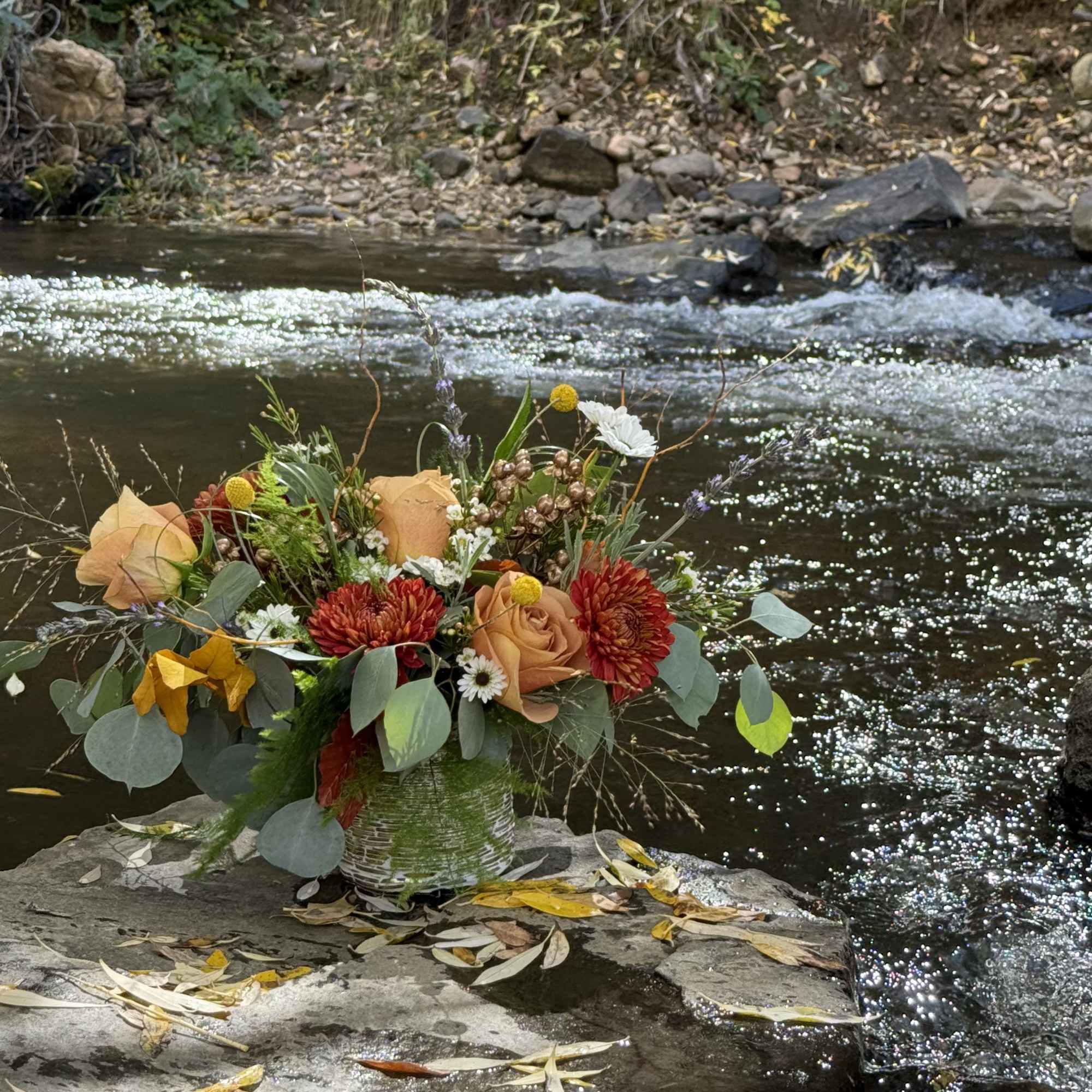 Autumn flower arrangement in a white vase beside a stream