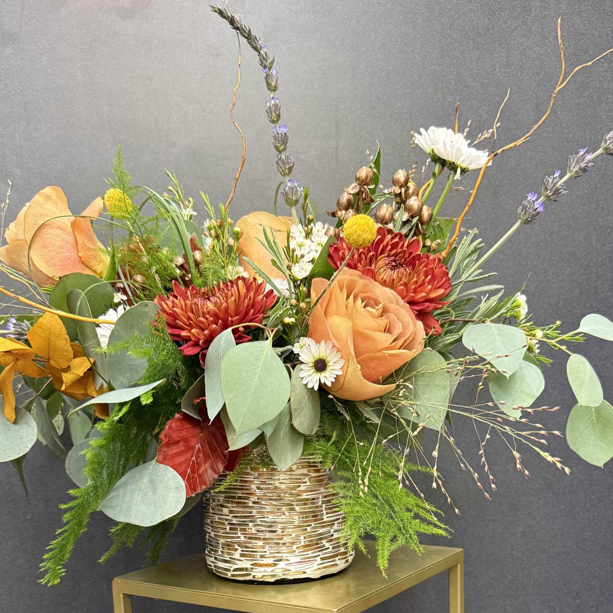 Autumn floral arrangement with orange roses and red mums in a woven vase