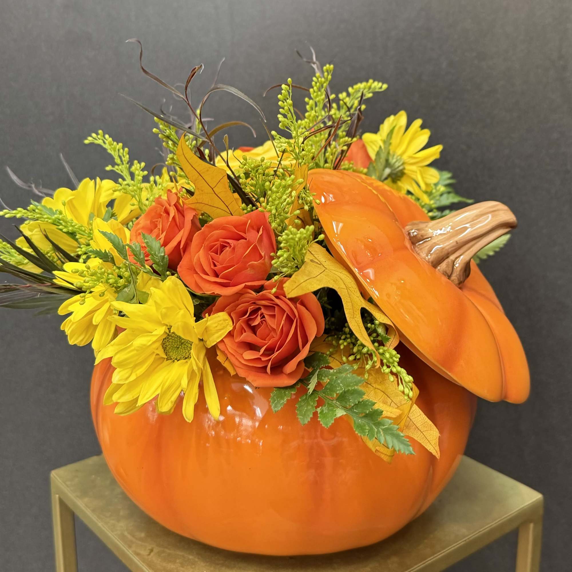Orange pumpkin container filled with yellow daisies and orange roses