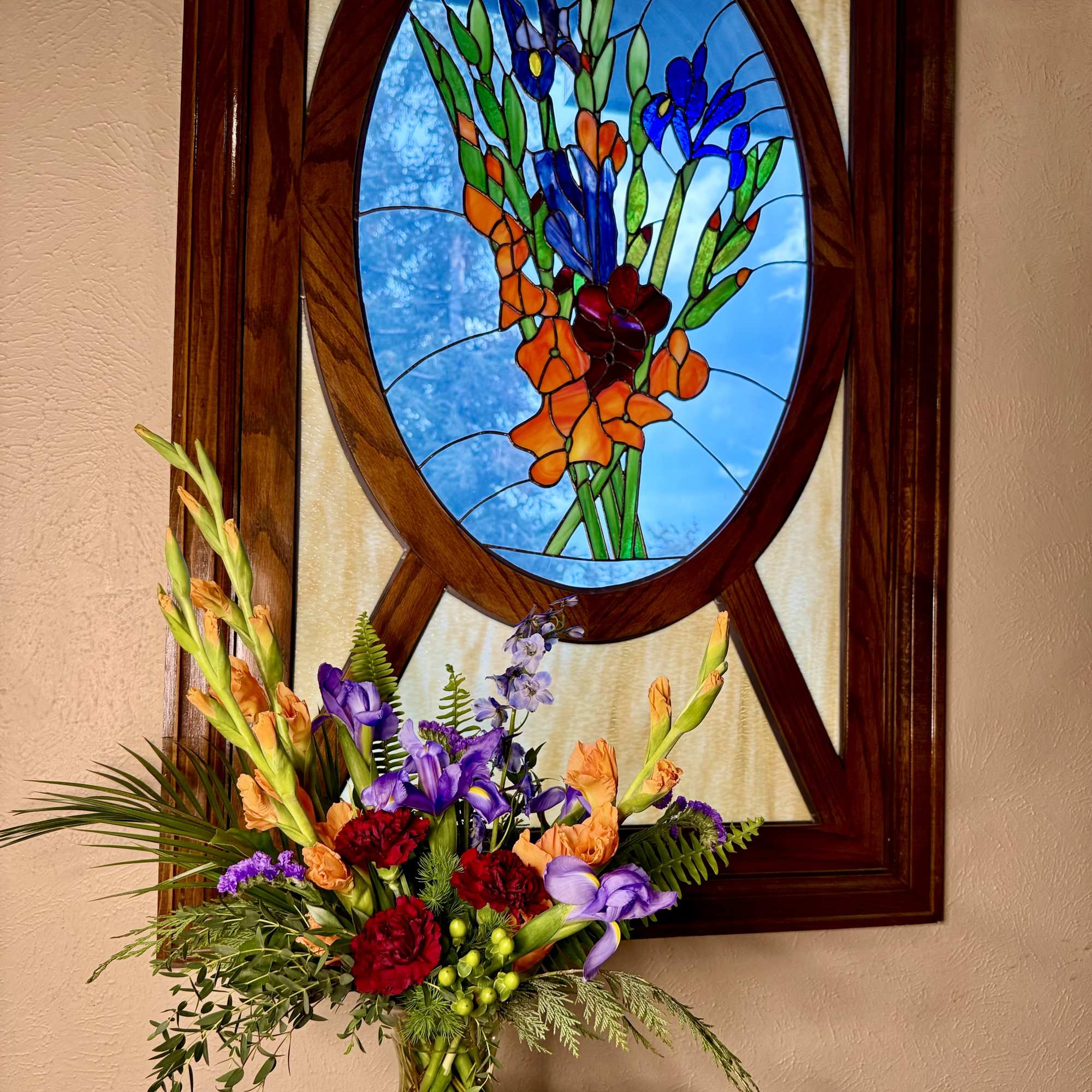 Colorful mixed flower arrangement in a glass vase beneath a stained-glass window