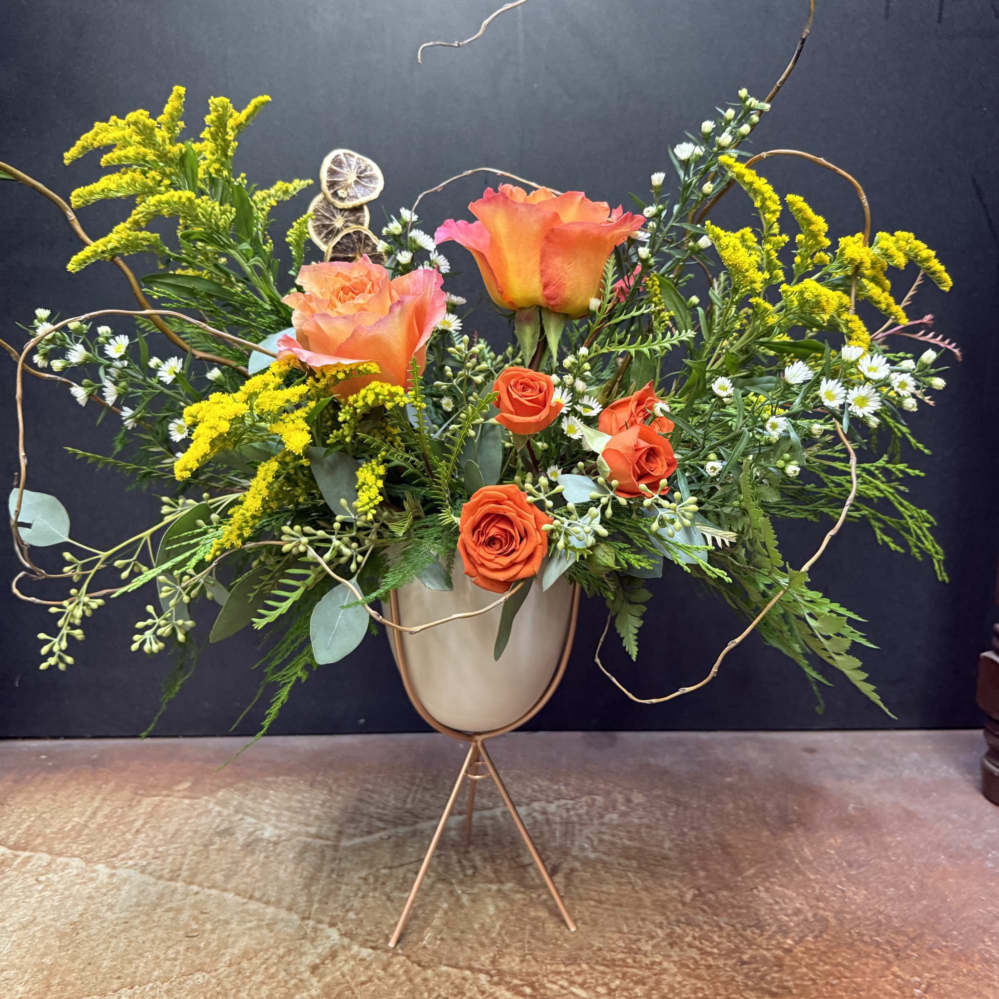 Orange roses and yellow filler flowers in a tall vase arrangement