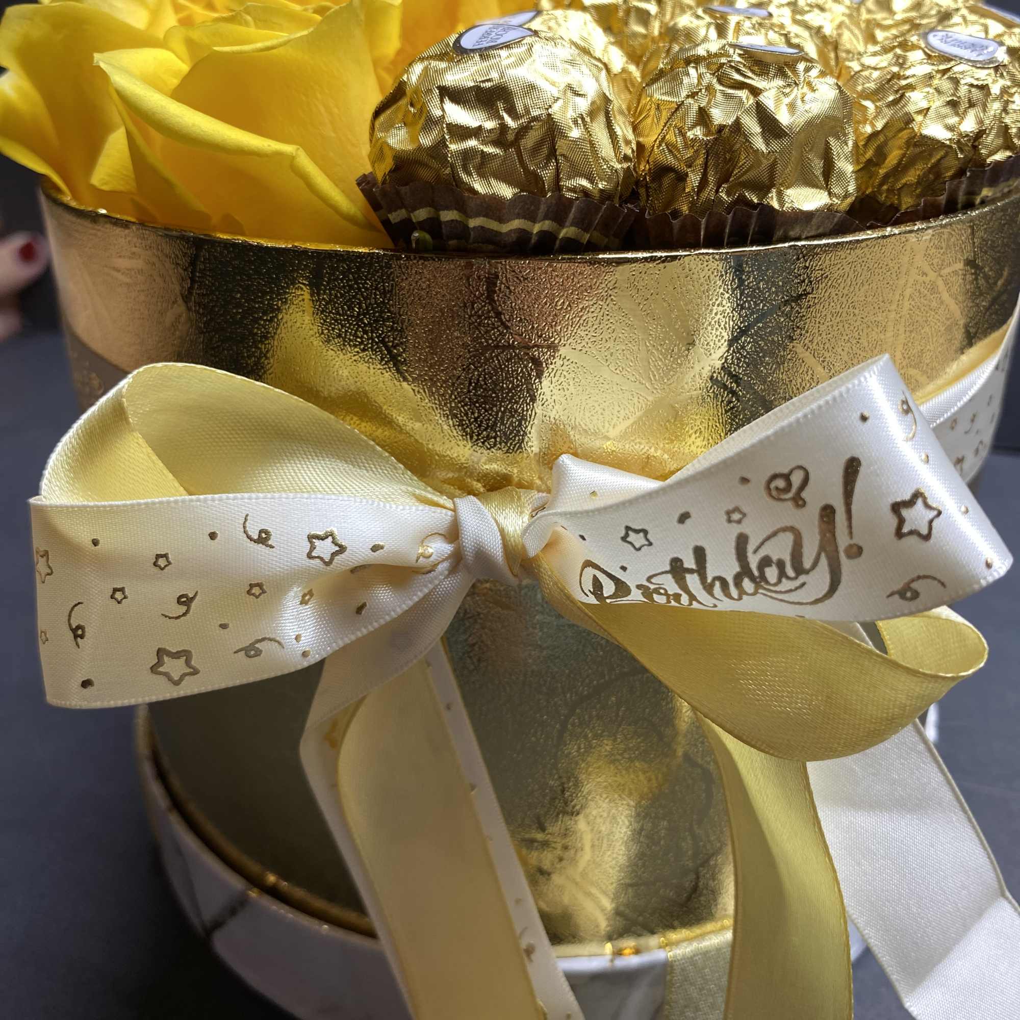 Yellow roses and gold-wrapped chocolates in a round gift box
