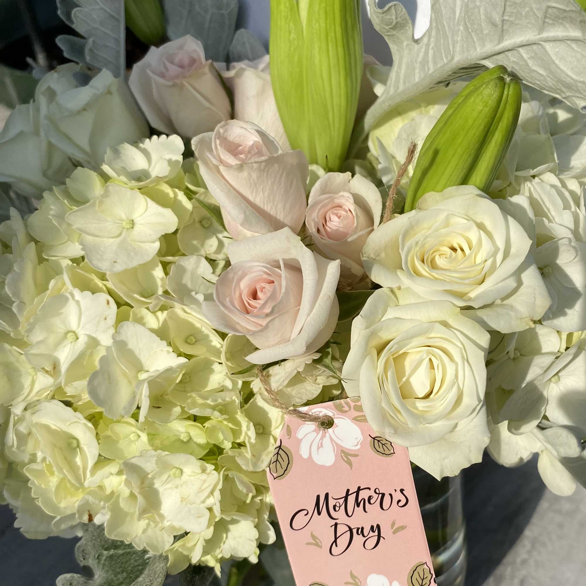 White roses and pale hydrangeas with green lily buds in a glass vase