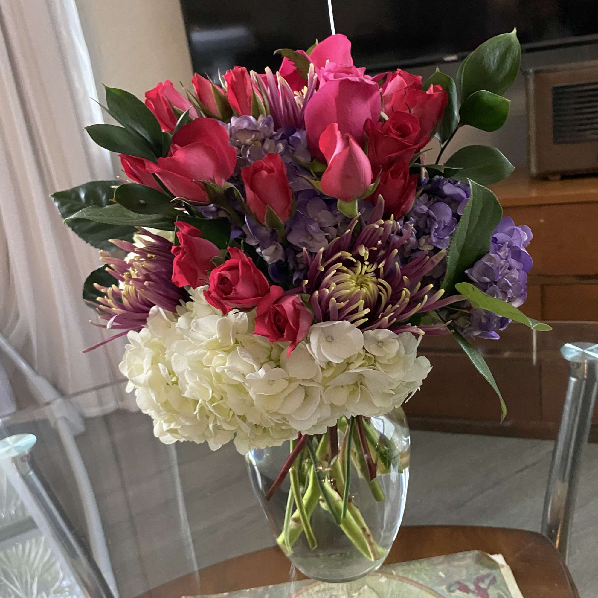 Bouquet of pink roses, purple blooms, and white hydrangeas in a glass vase