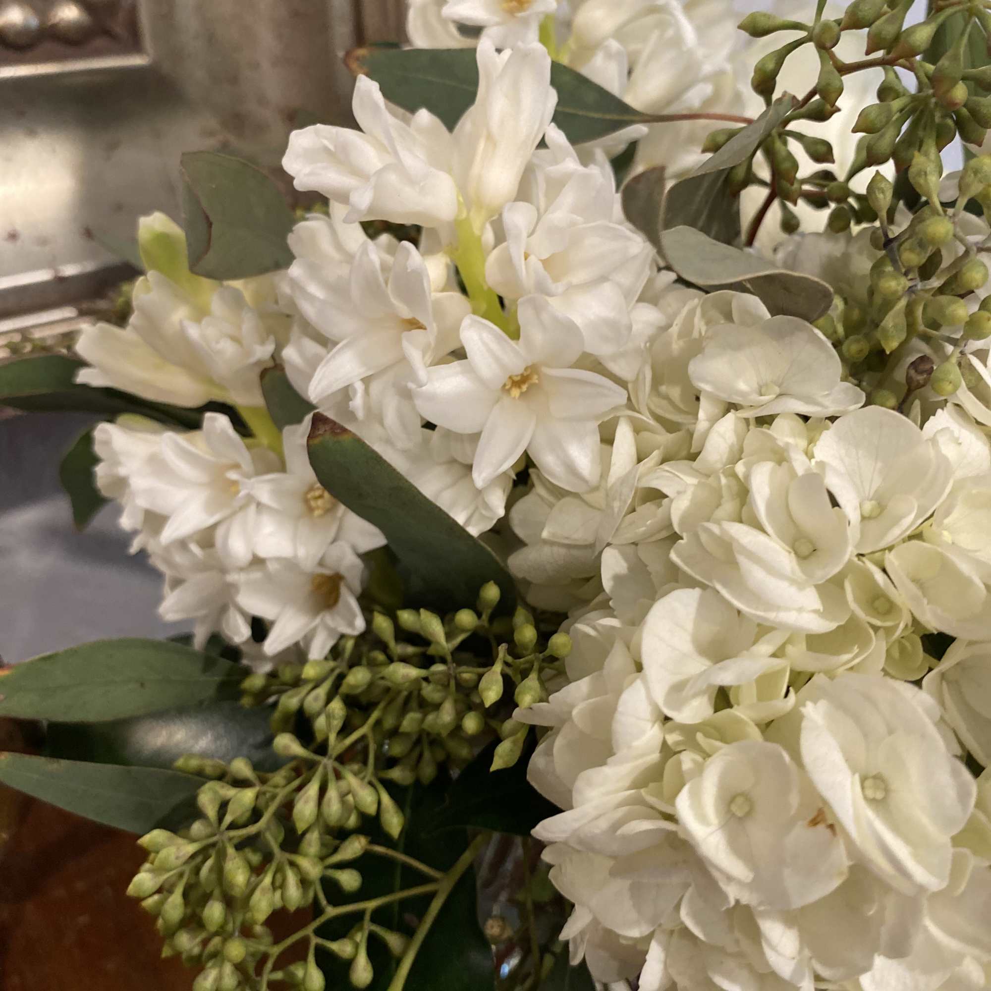 White flowers and hydrangea blooms arranged with greenery in a vase