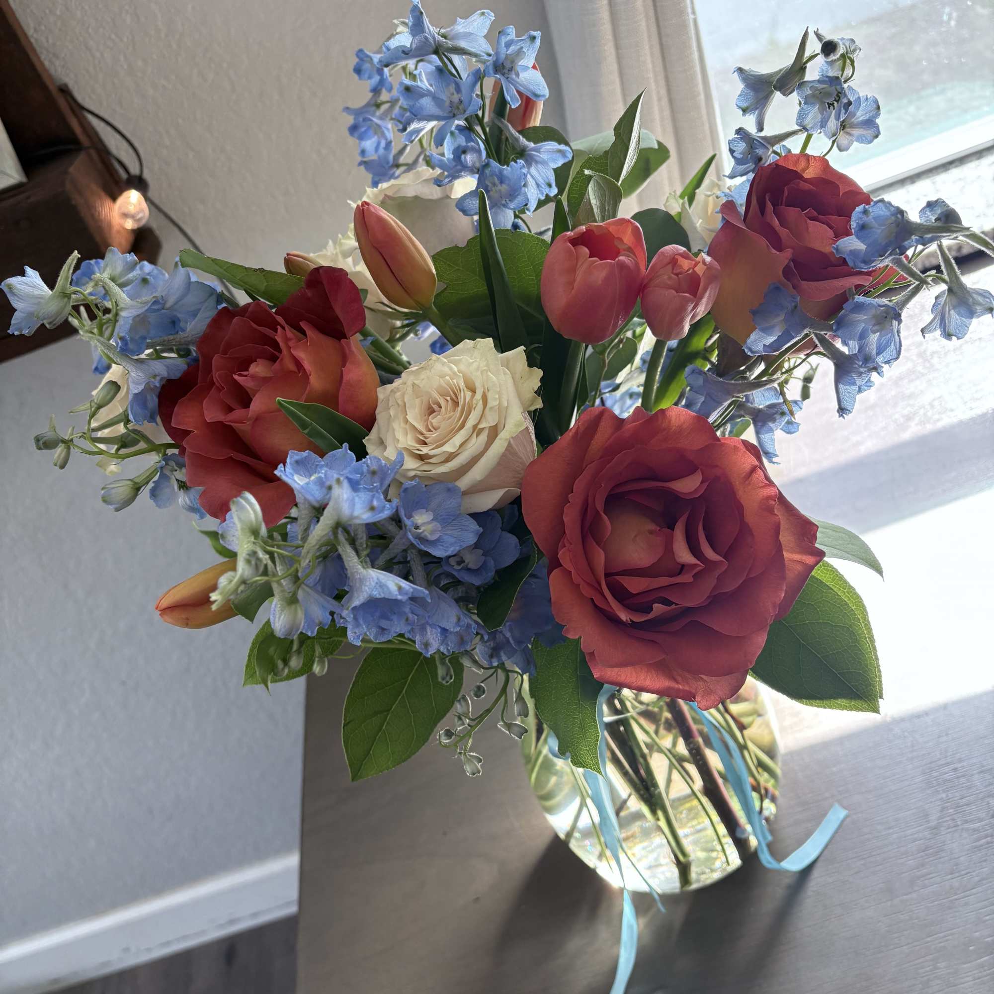 Bouquet of red roses, pink tulips, and blue flowers in a glass vase