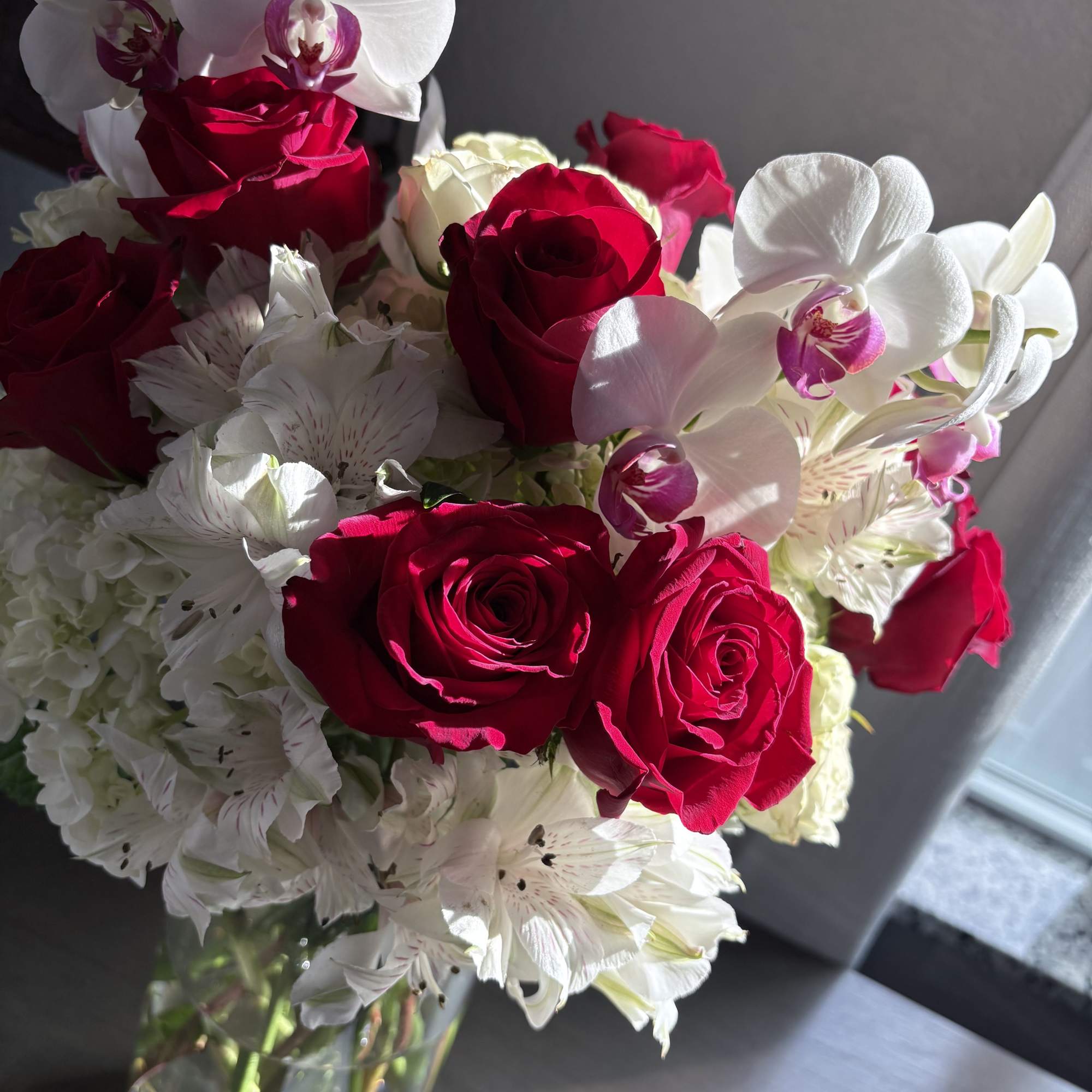 Bouquet of red roses, white orchids, and white alstroemeria in a glass vase