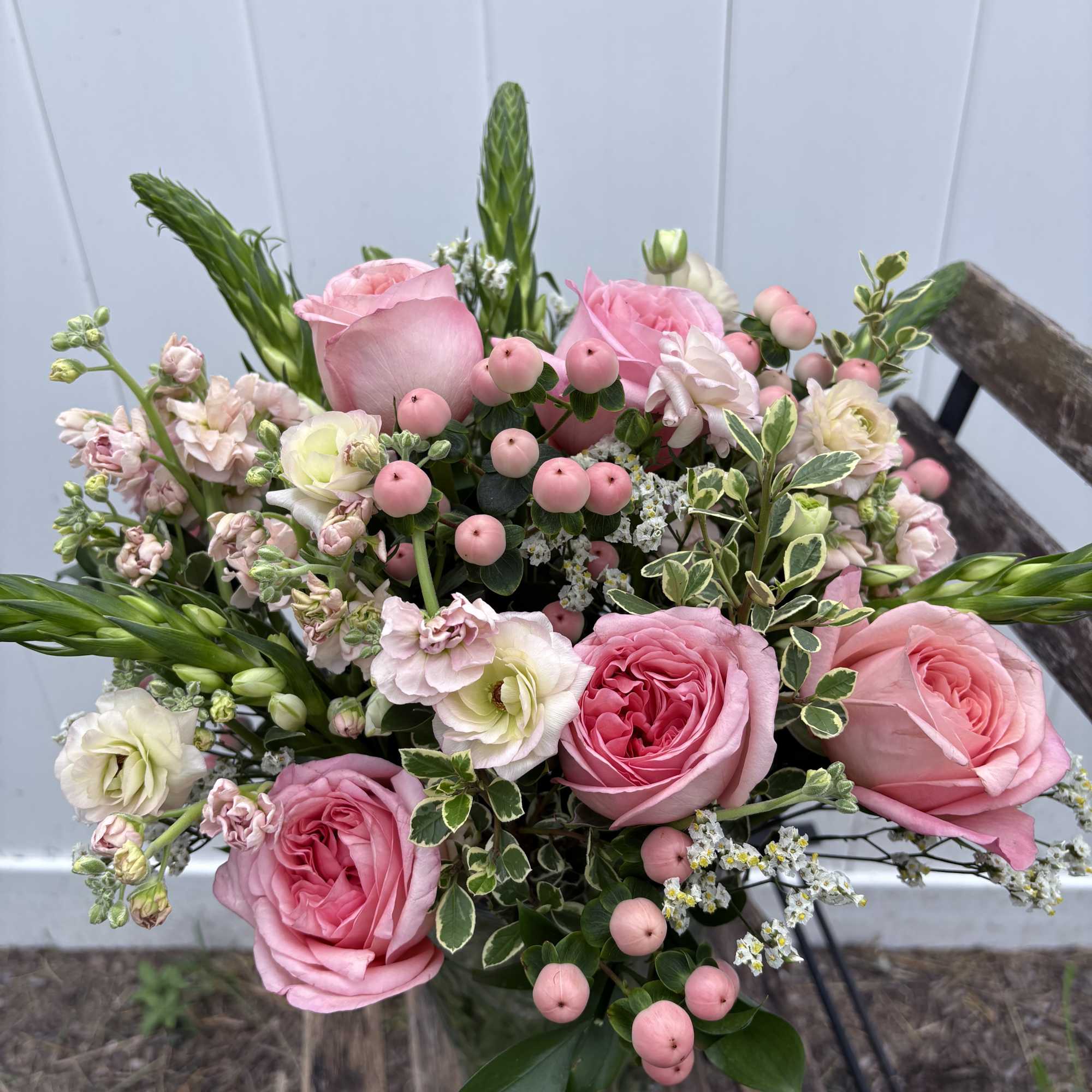 Pink roses and pale blooms arranged in a glass vase with pink berries