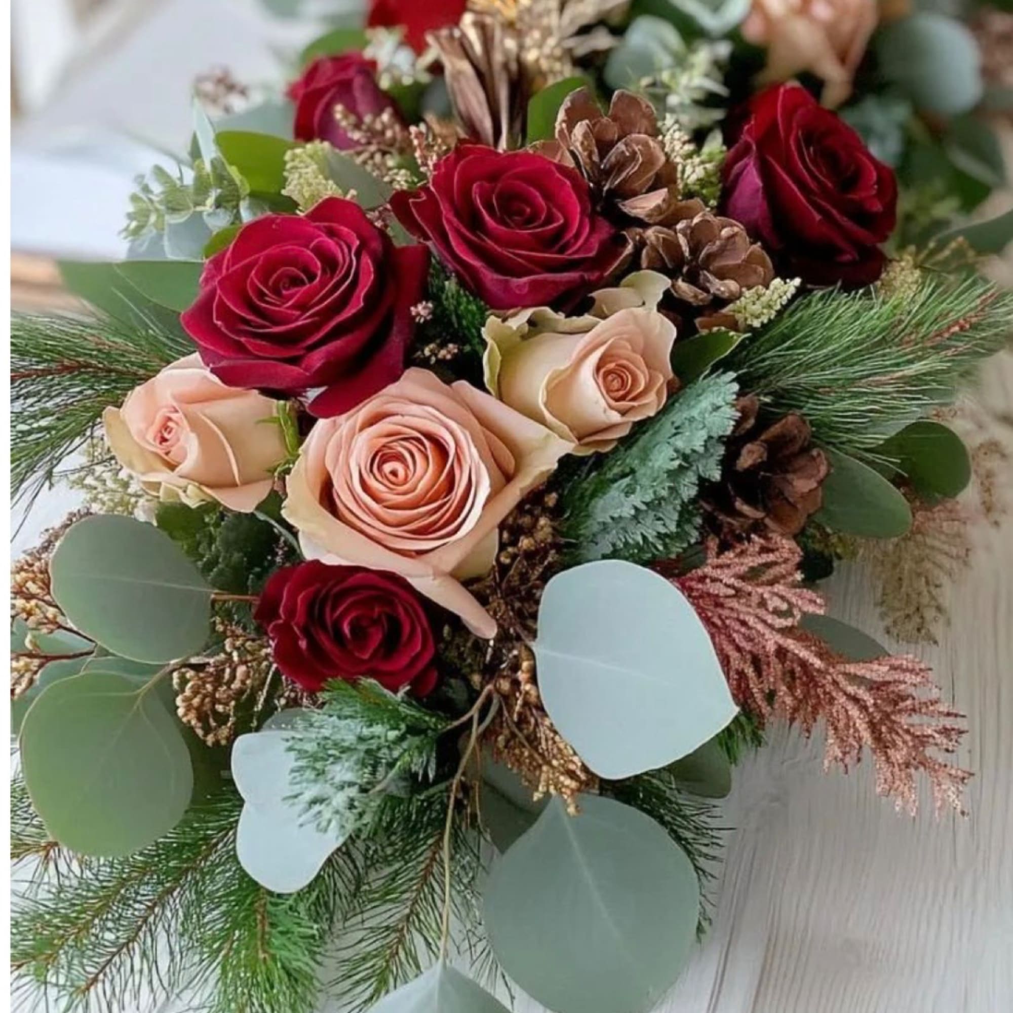 Bouquet of red and blush roses with pinecones and greenery