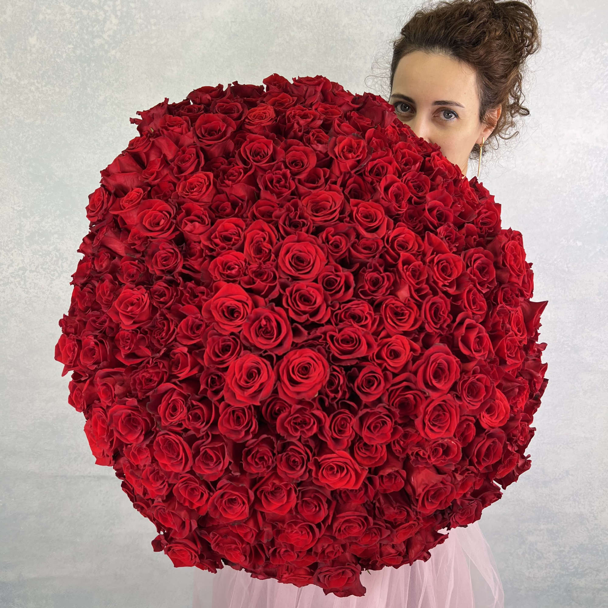 Oversized round bouquet of tightly packed red roses held in front of a woman's face.