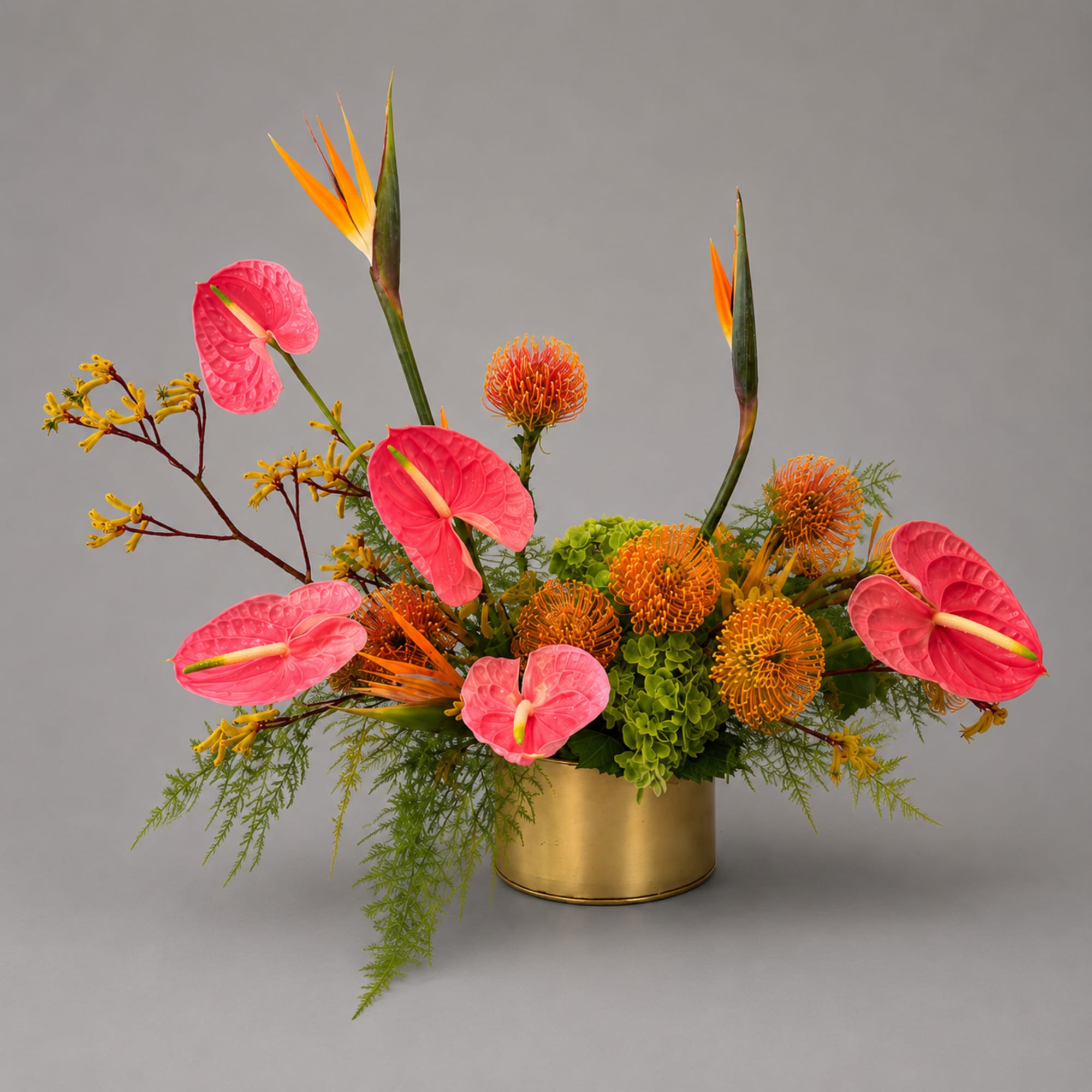 Tropical flower arrangement with pink anthuriums and orange blooms in a gold container