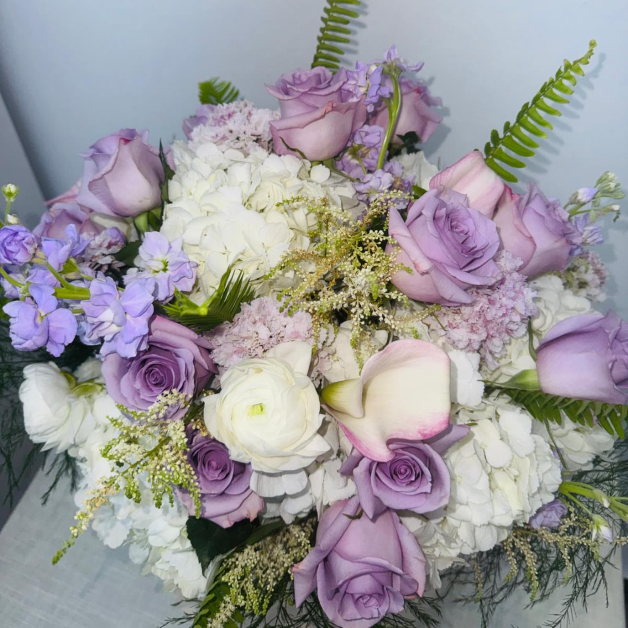 Lavender roses and white blooms arranged in a bouquet with calla lilies