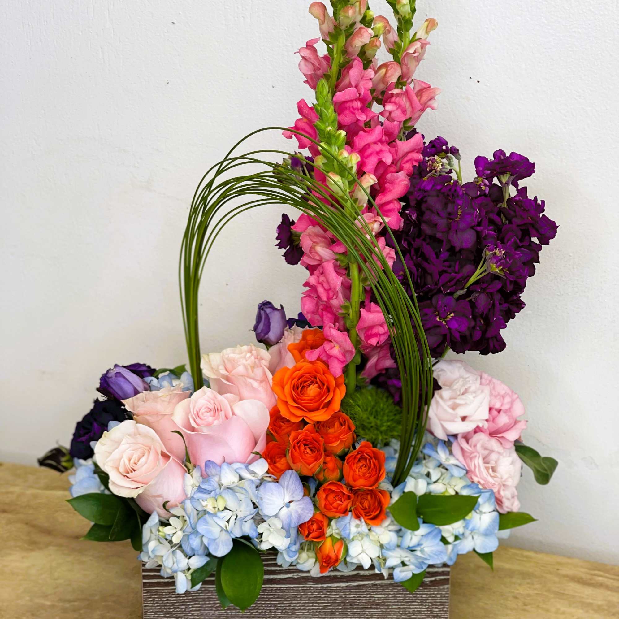 Colorful floral arrangement in a rectangular box with roses and tall pink spikes