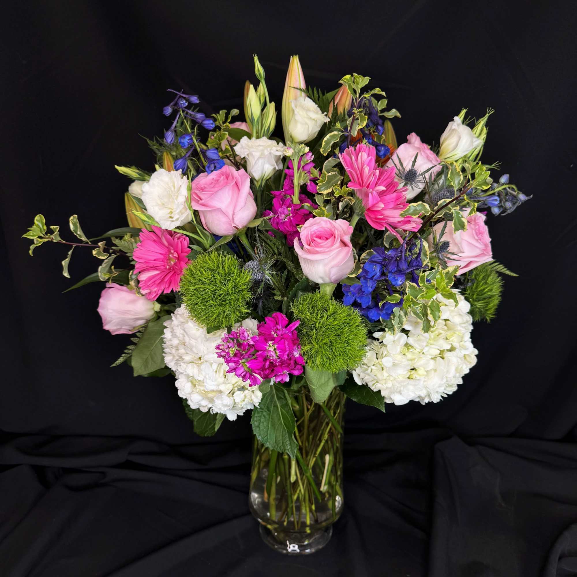 Mixed bouquet of pink roses, white hydrangeas, and blue flowers in a glass vase