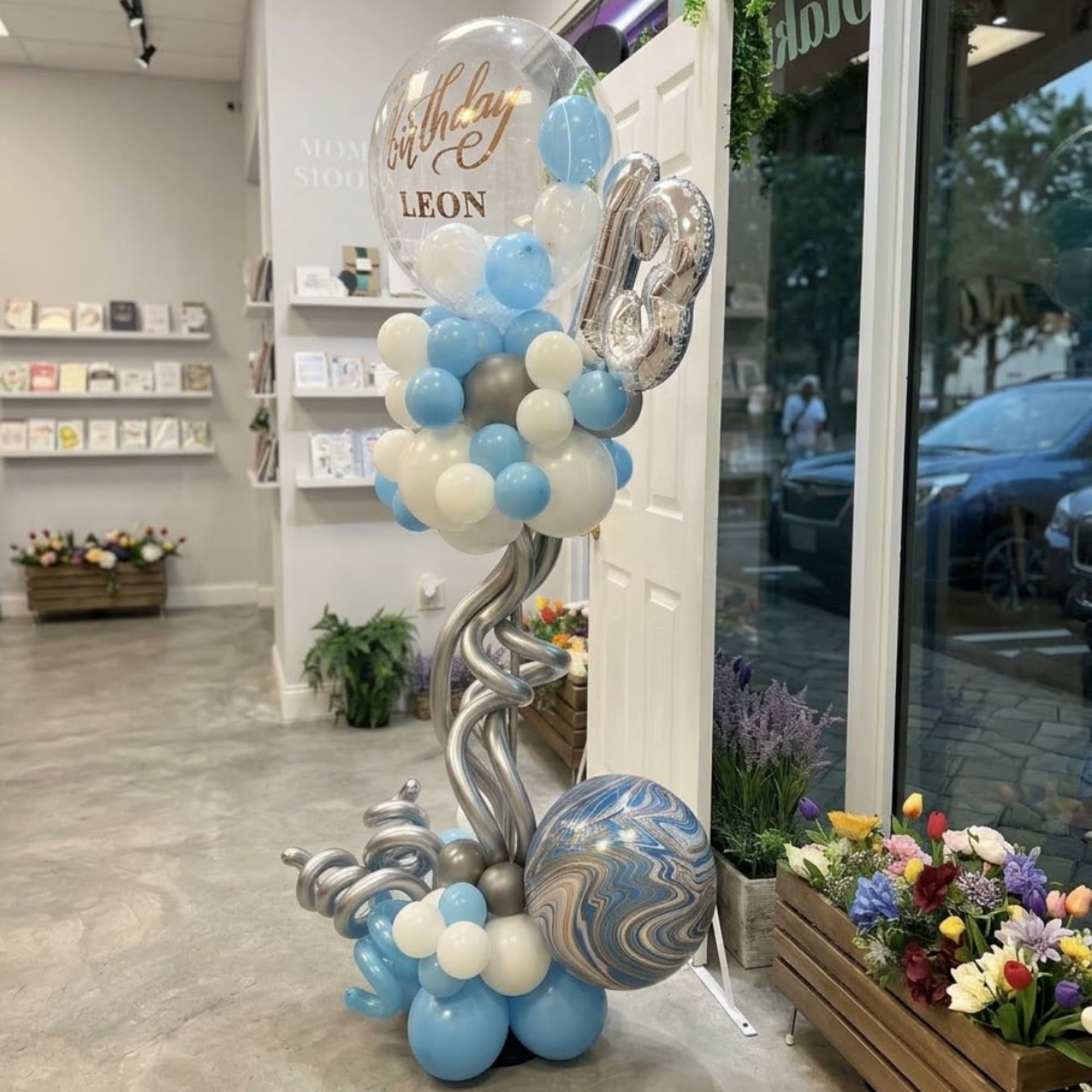 Birthday balloon display with a clear balloon, silver number 18, and blue-white balloons
