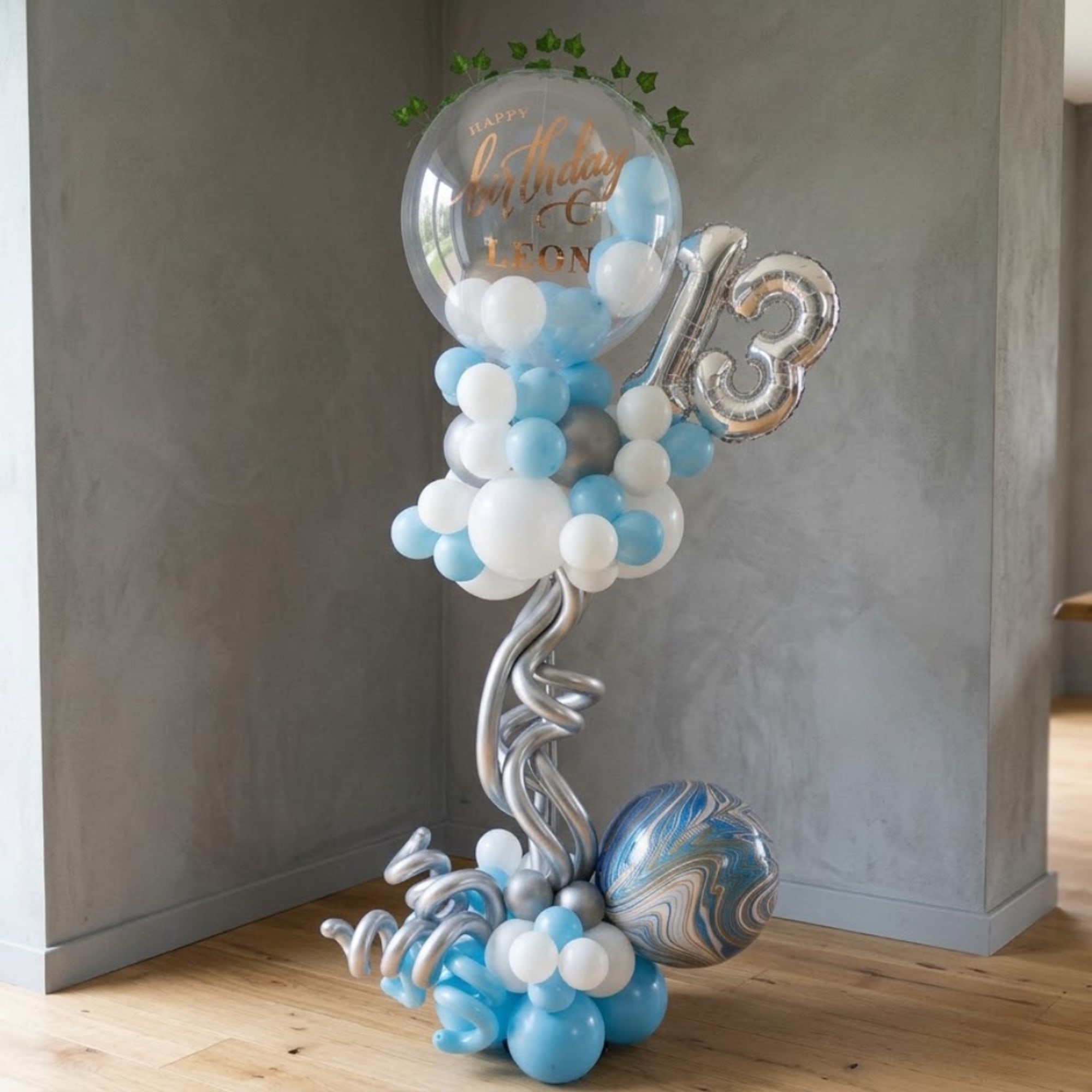 Birthday balloon arrangement with blue, white, and silver balloons and a clear topper