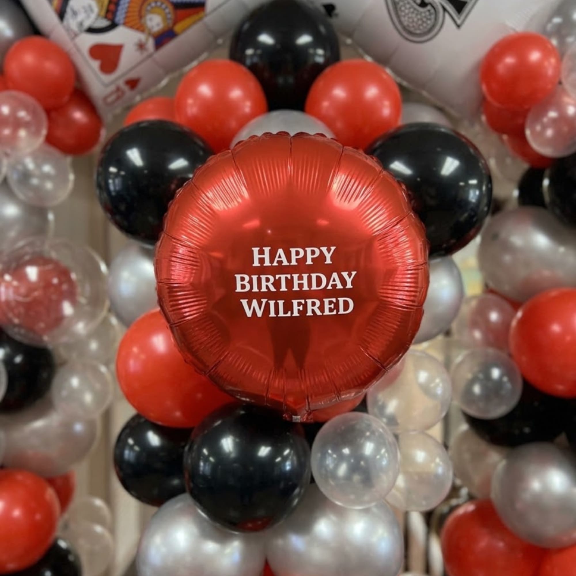 Red birthday balloon with black, silver, and clear balloons around it