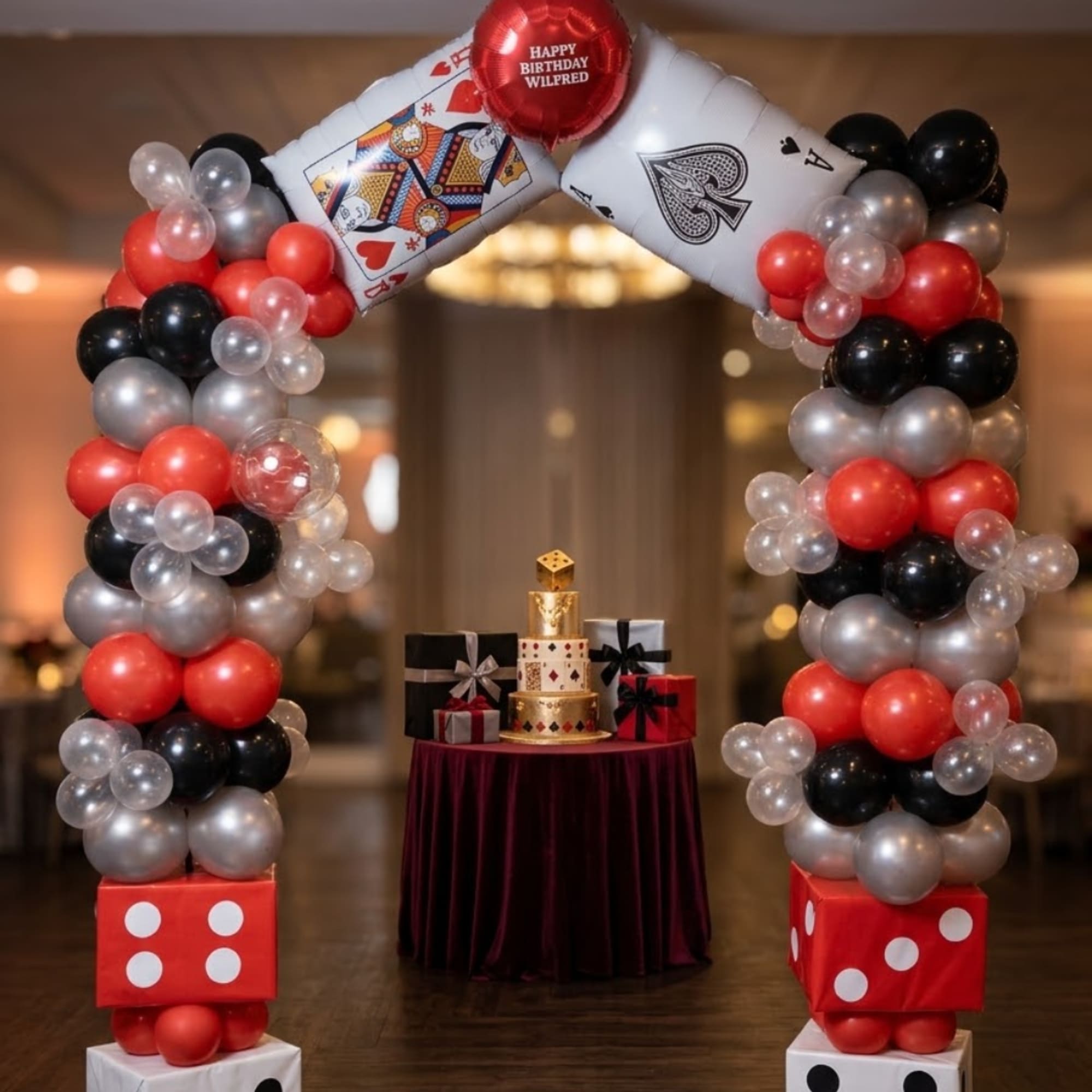 Balloon arch with playing-card decorations and birthday balloons over a gift table