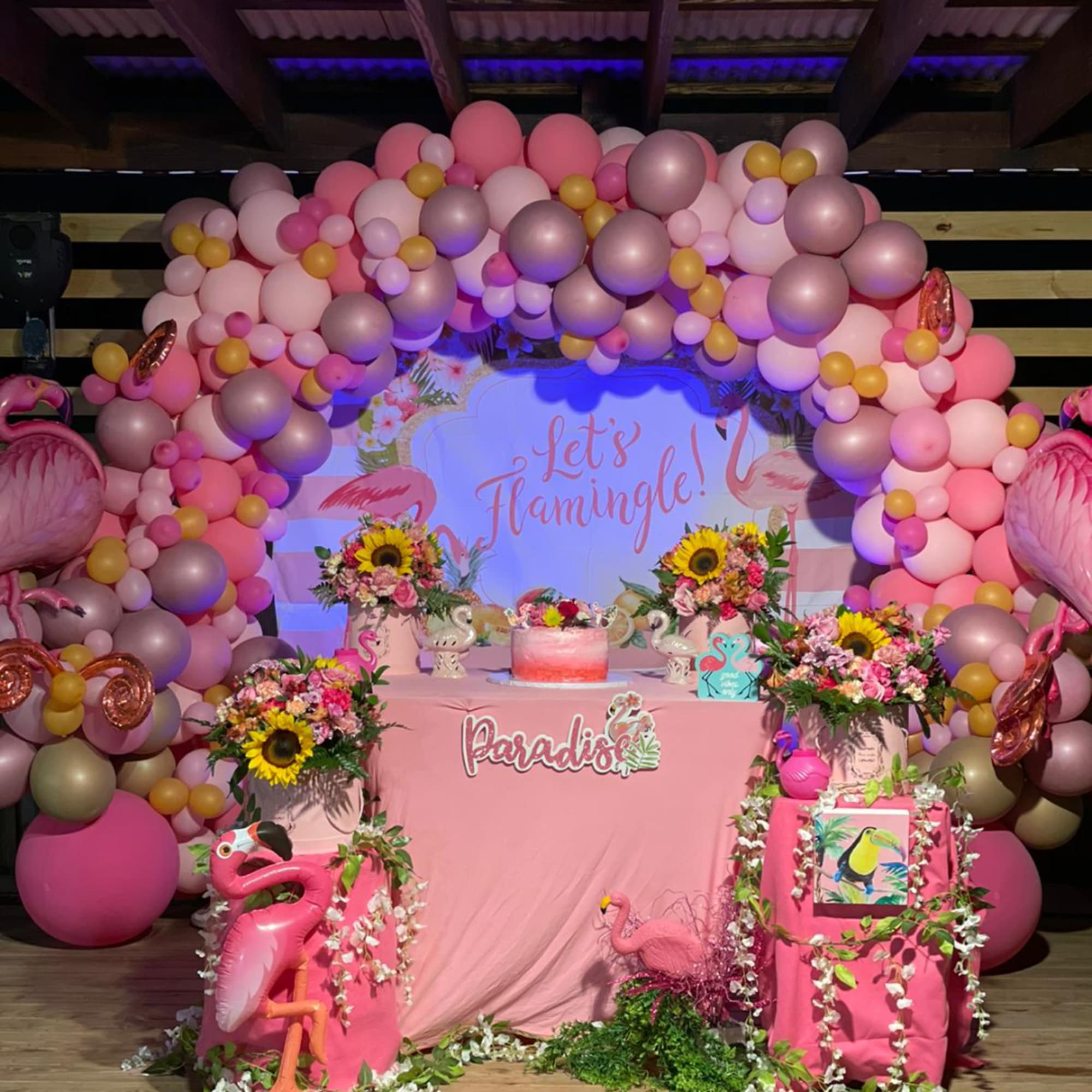 Pink floral arrangements and balloons around a flamingo-themed party display