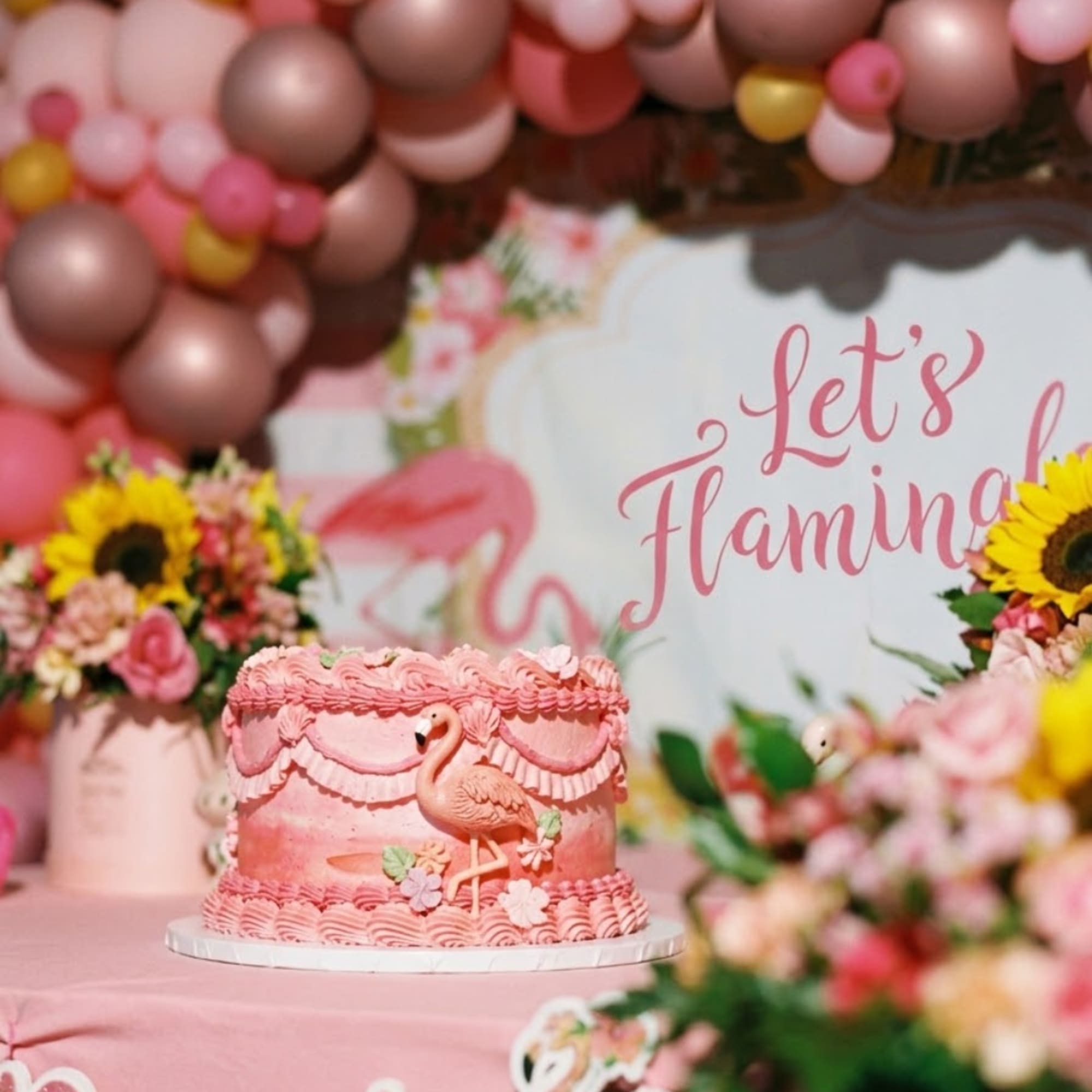 Pink flamingo cake on a table with balloon decor and floral arrangements