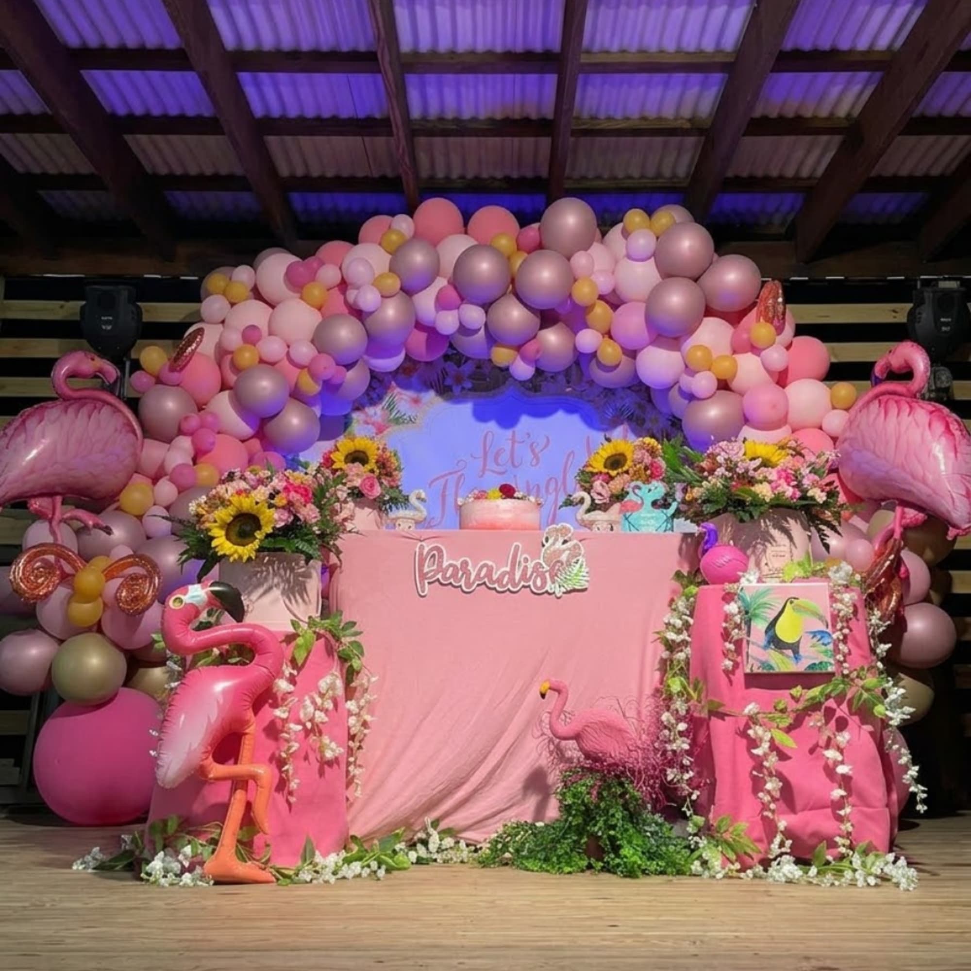 Pink balloon arch with floral arrangements and flamingo decorations around a party table, photo 7 of 7