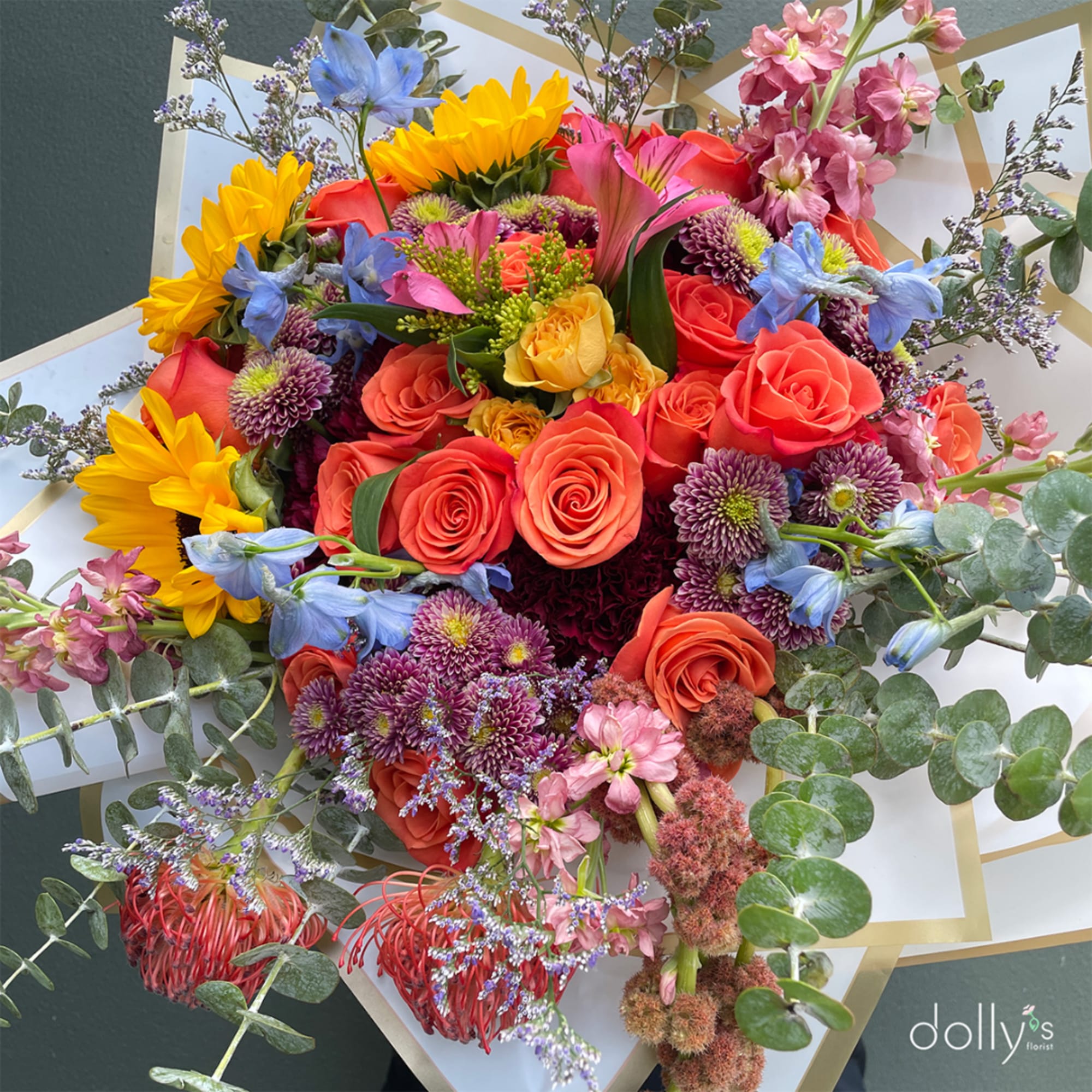 Colorful bouquet with roses, sunflowers, and blue flowers in white wrap