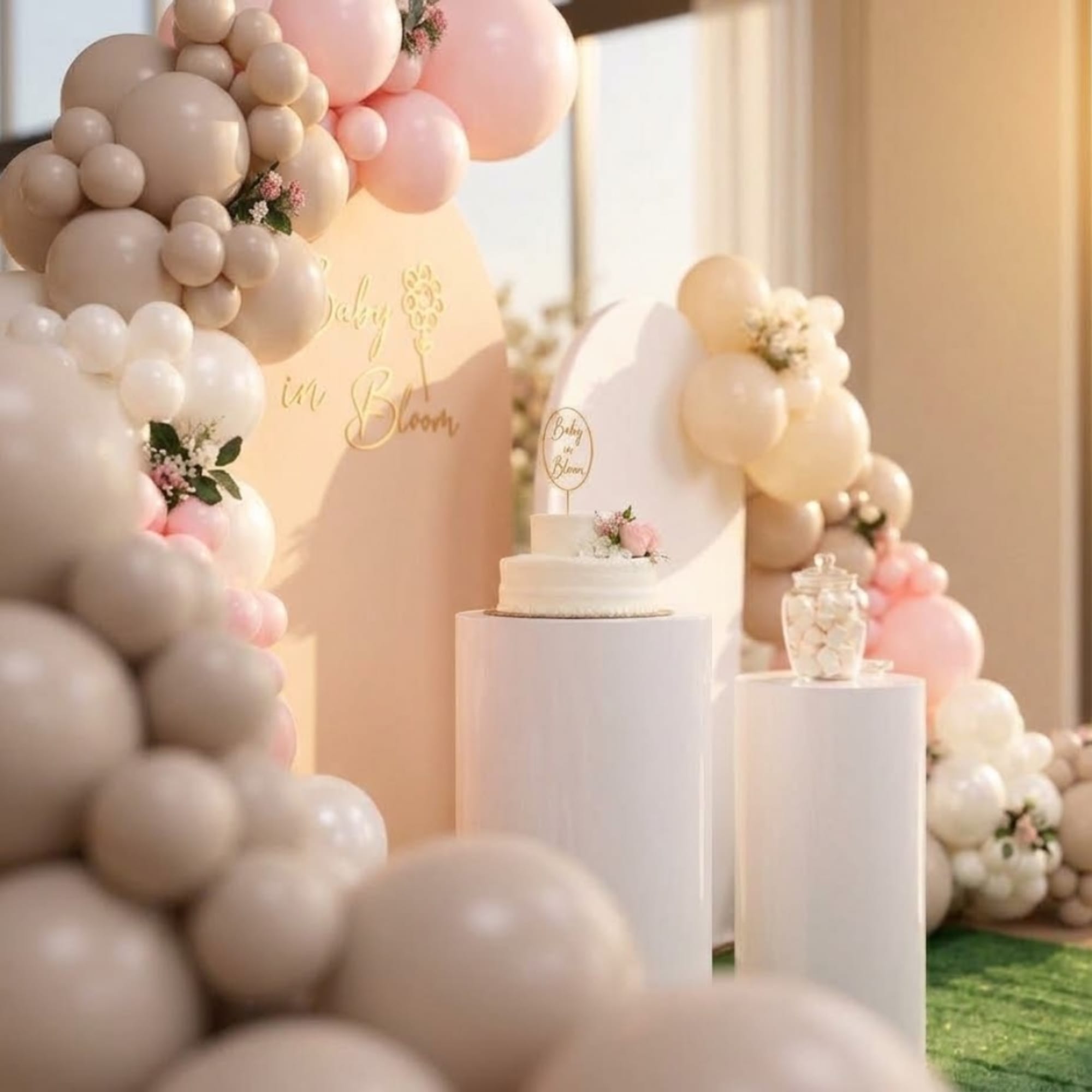 Pastel balloon arch with a small cake on white pedestals