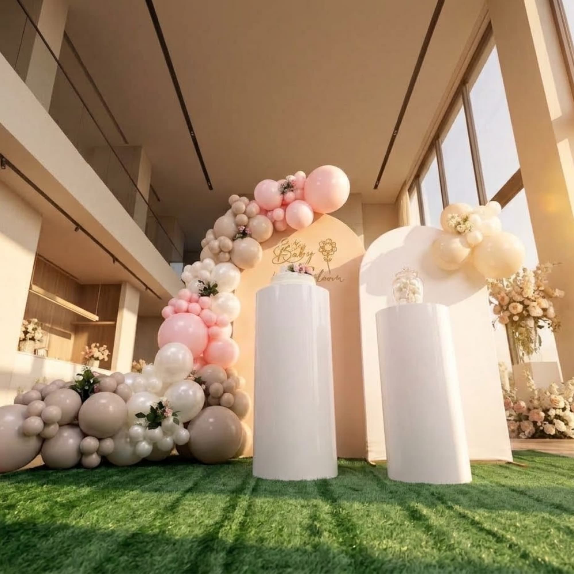 Pastel balloon arch with floral accents around white display pedestals