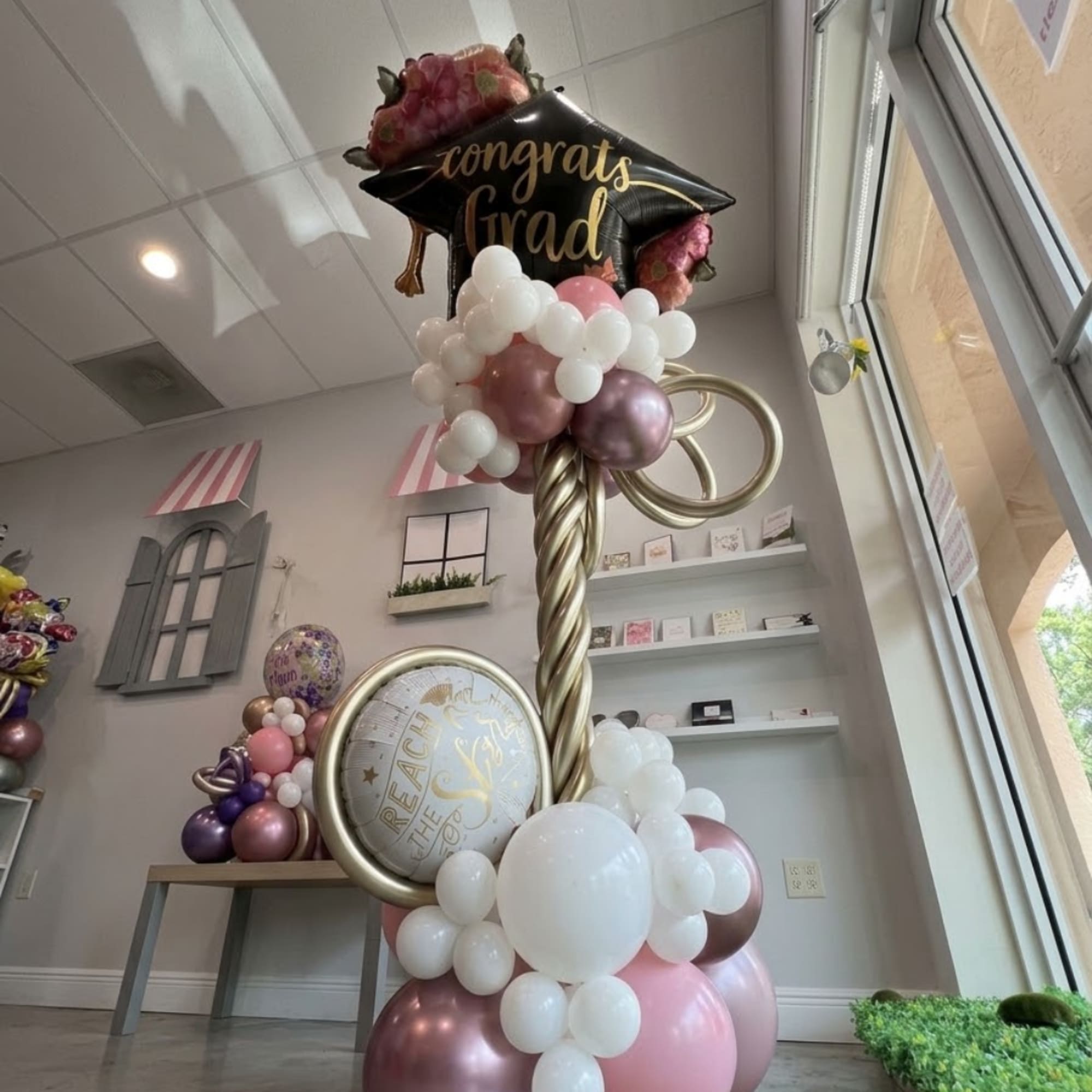 Graduation balloon display with pink and gold balloons and a black congrats grad topper