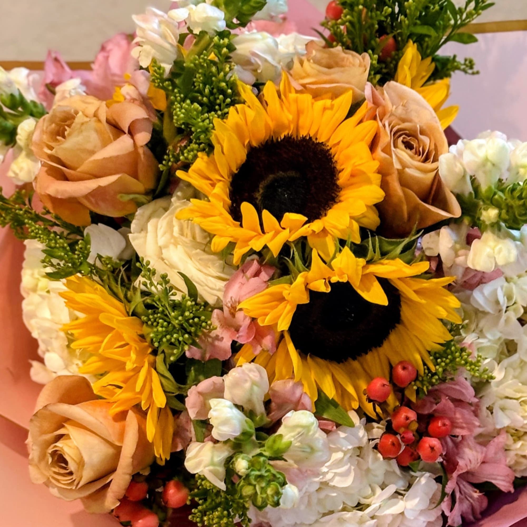 Bouquet of sunflowers, roses, and white blooms in pink wrapping