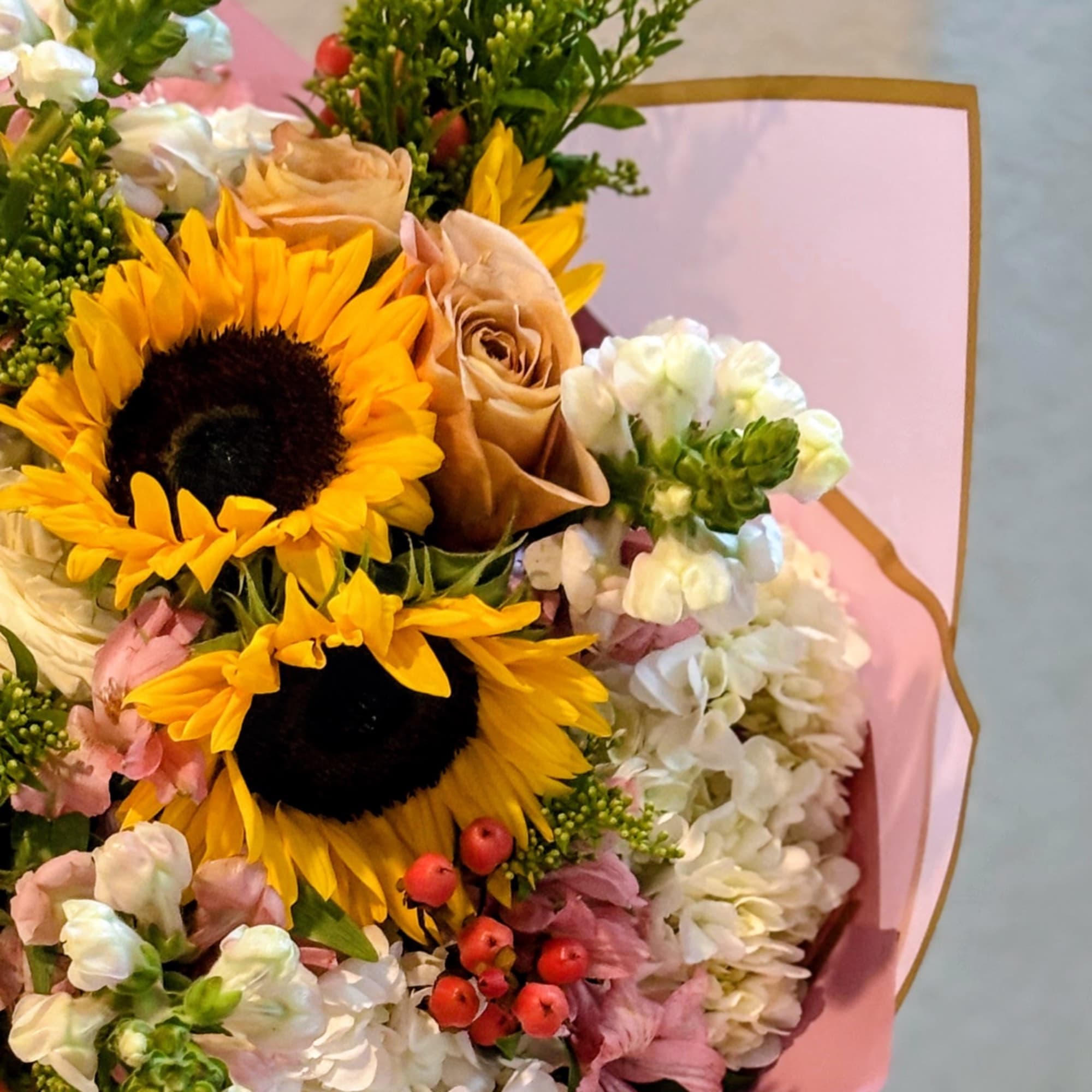 Bouquet with sunflowers, roses, and white blooms wrapped in pink paper