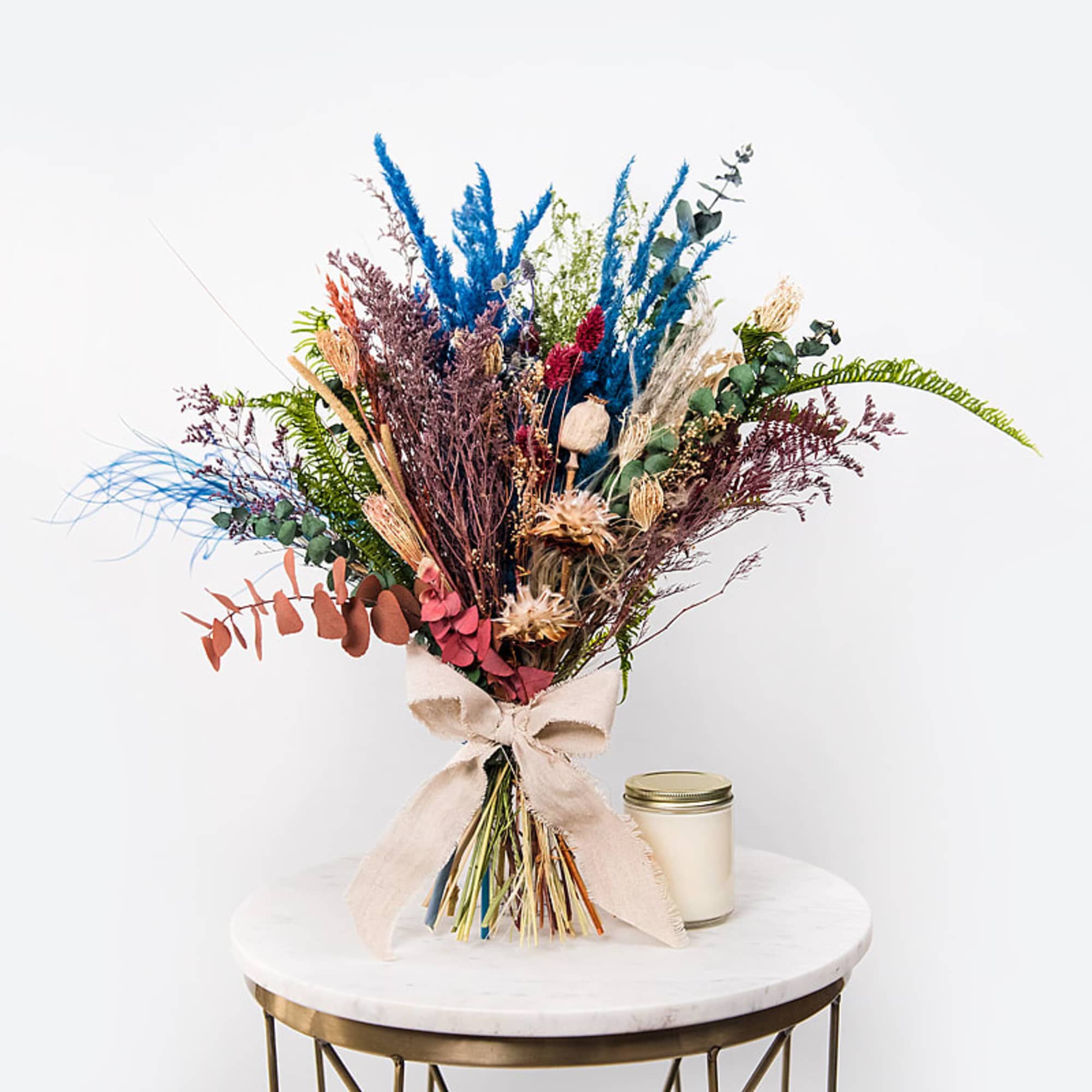 Dried flower bouquet with a beige ribbon beside a small candle jar