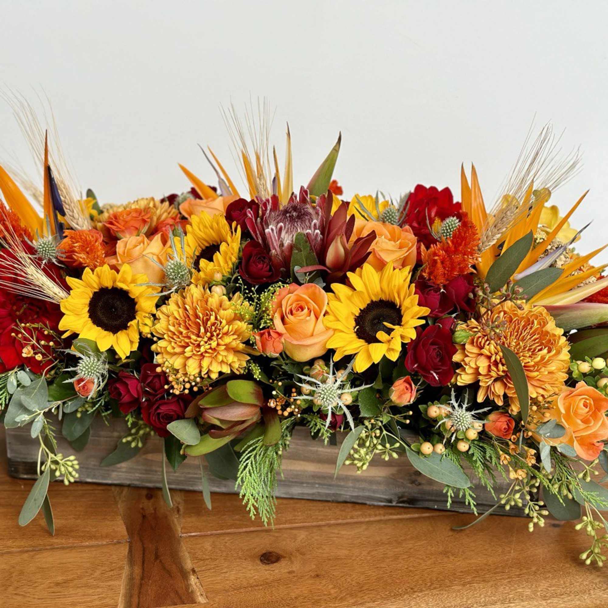 Long low arrangement of sunflowers, roses, and orange blooms in a rectangular container