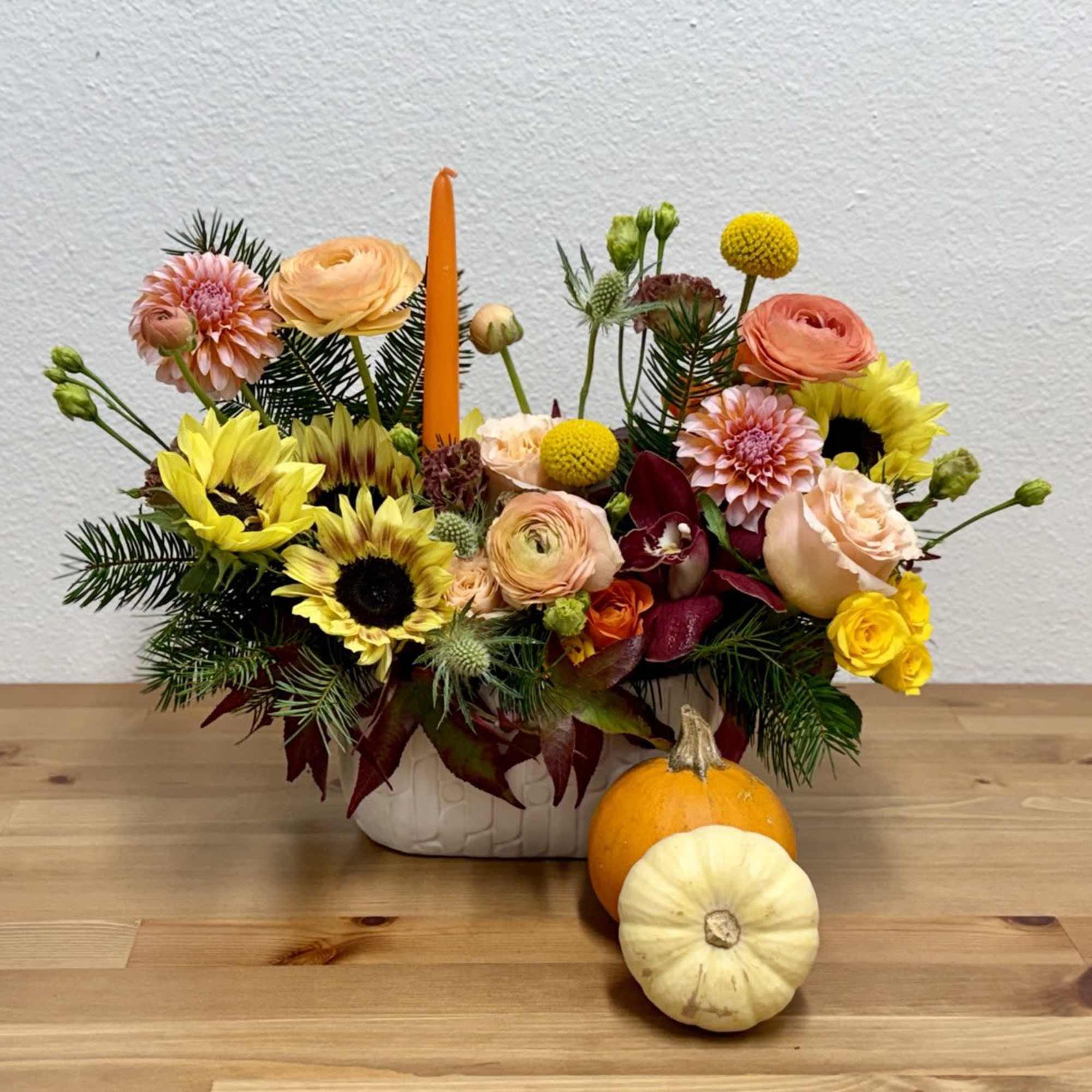 Autumn floral arrangement in a white vase with pumpkins in front