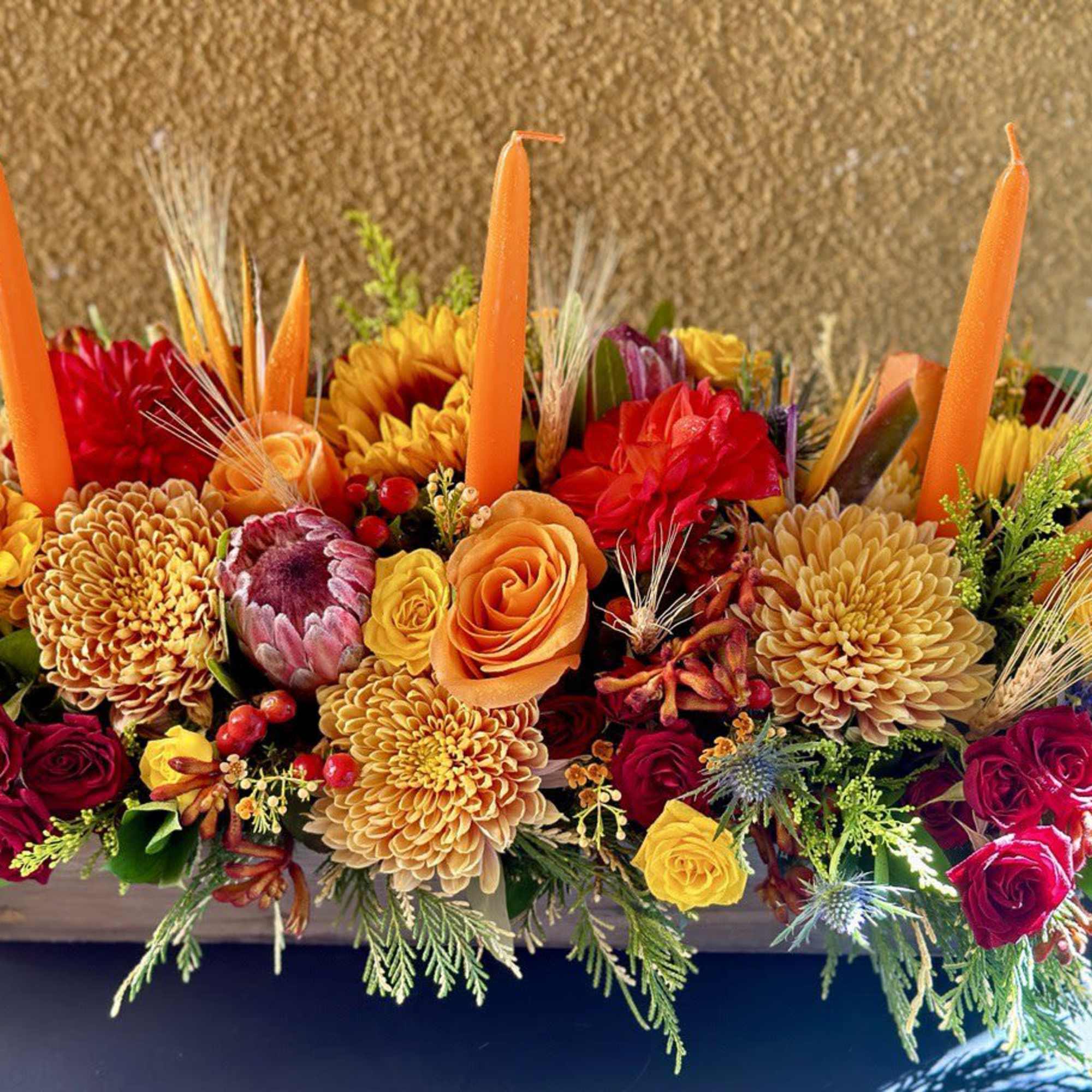 Bright autumn floral centerpiece with sunflowers, roses, and orange candles in a low container