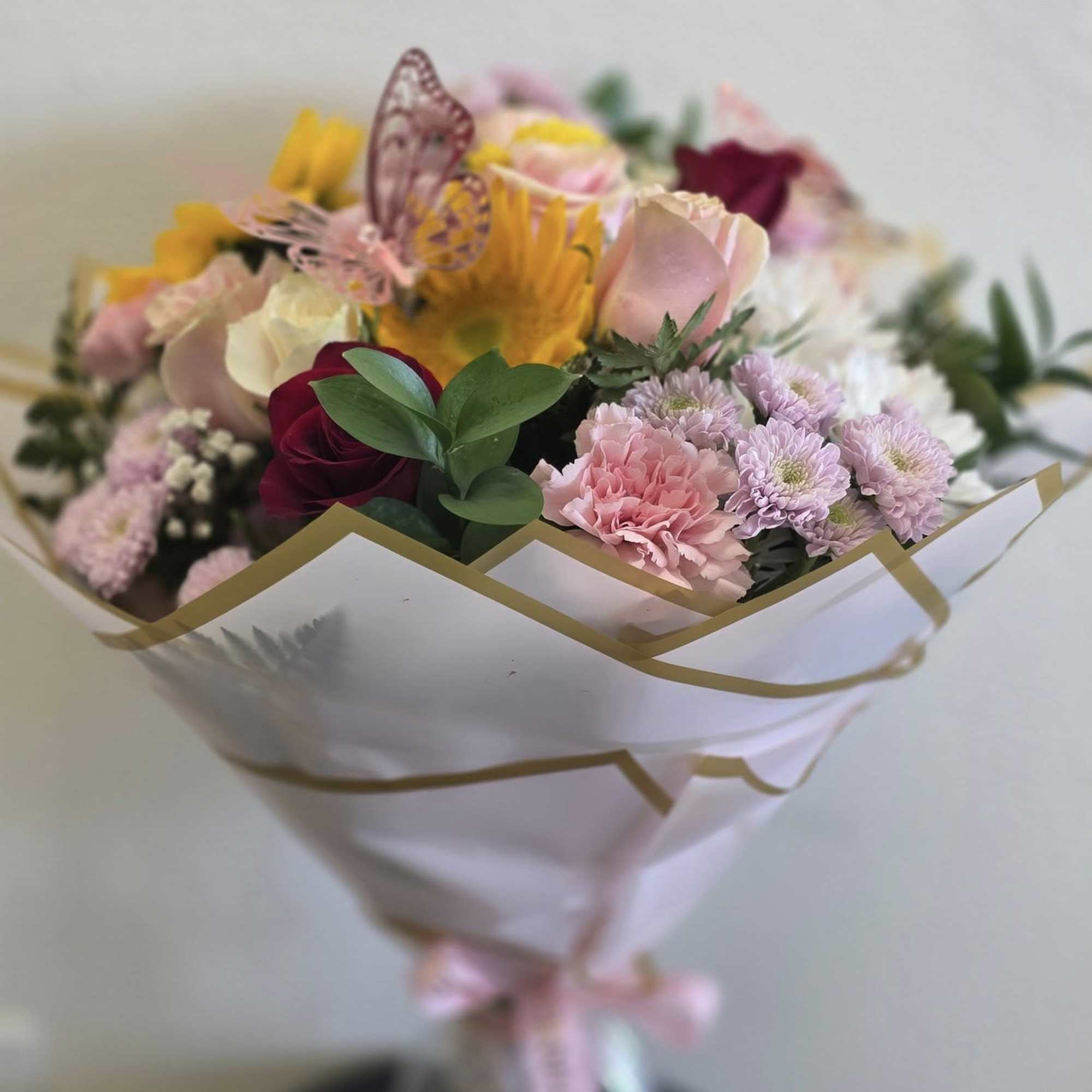 Mixed bouquet of pink, yellow, and white flowers wrapped in white paper