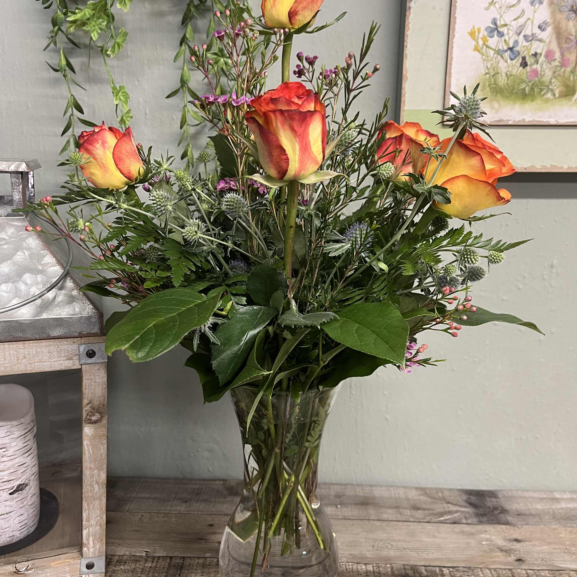 Orange-yellow roses in a clear glass vase with mixed greenery