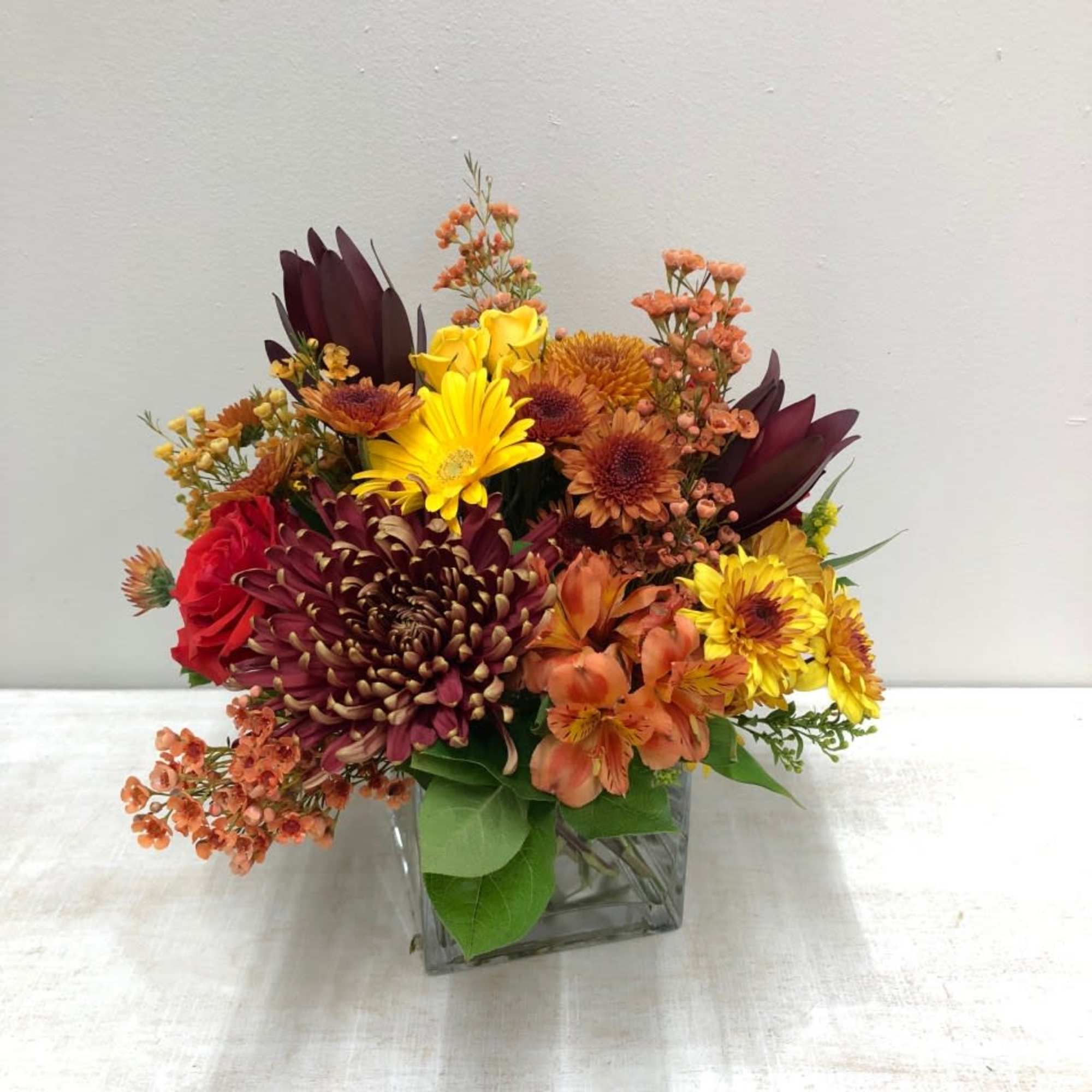 Mixed autumn bouquet in a square glass vase with red, yellow, and orange blooms