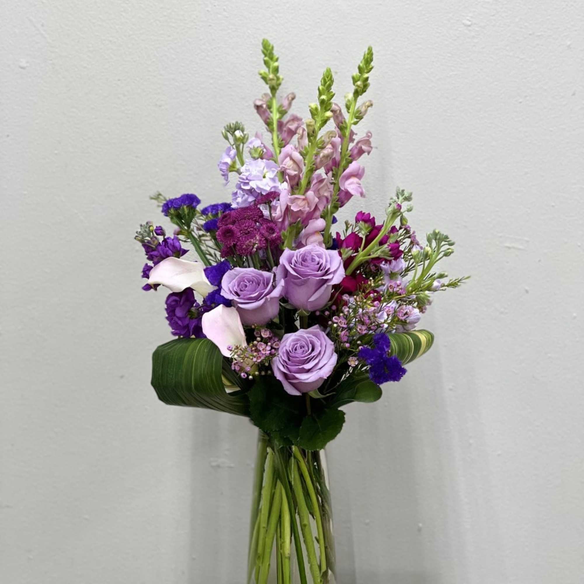 Lavender roses and purple mixed flowers in a clear glass vase