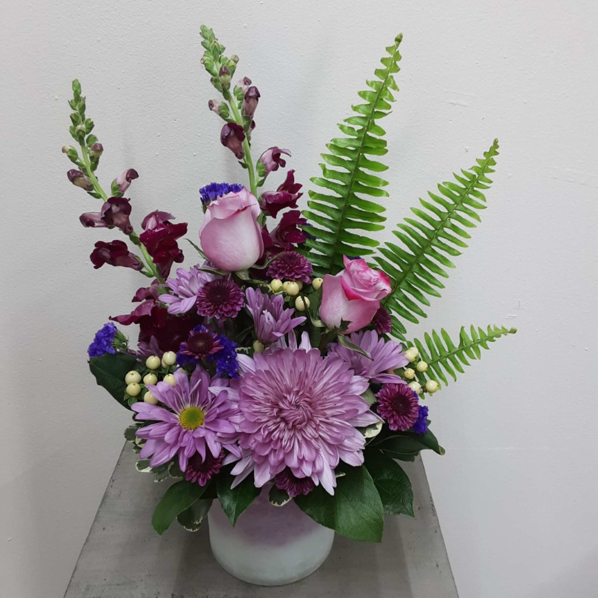 Lavender and pink floral arrangement in a white vase with fern fronds