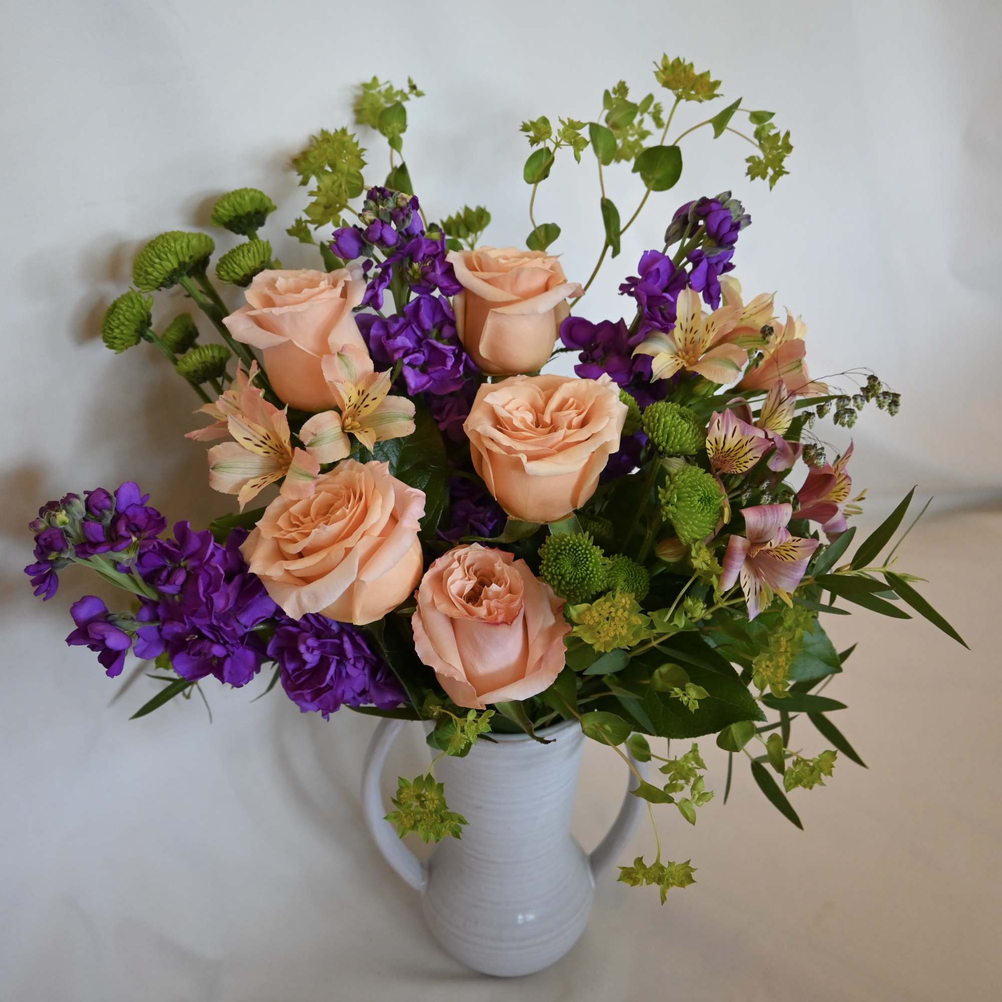 Peach roses and purple flowers in a white vase