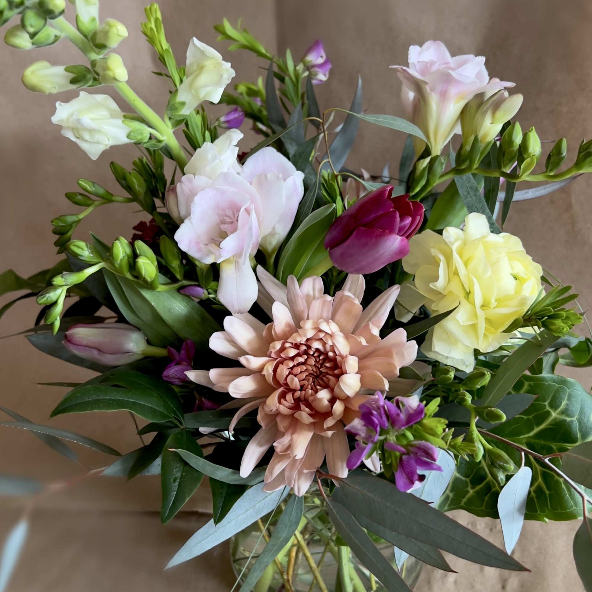 Mixed bouquet in a glass vase with pale pink, yellow, and purple blooms
