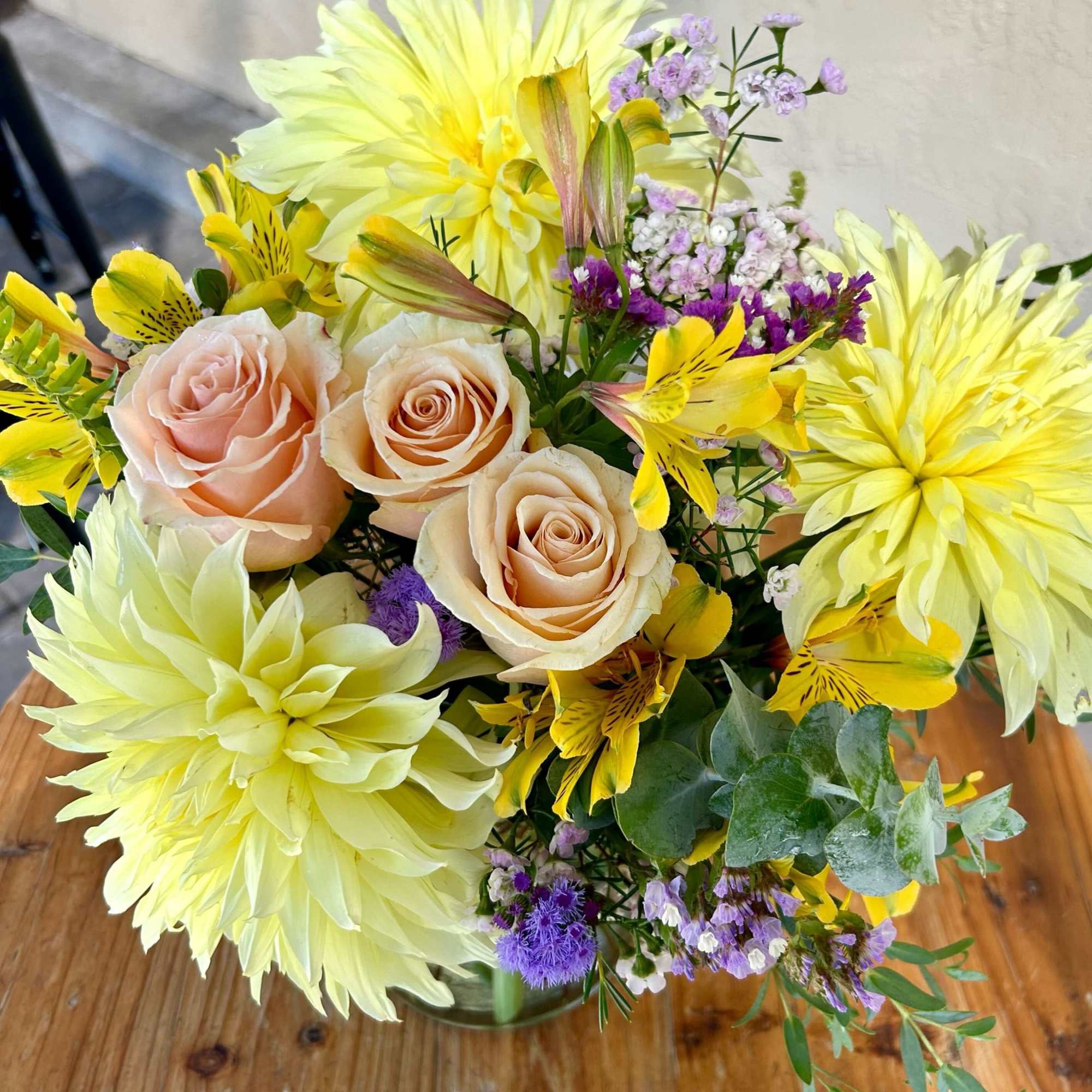 Bouquet of pale yellow dahlias, peach roses, and yellow alstroemeria in a glass vase